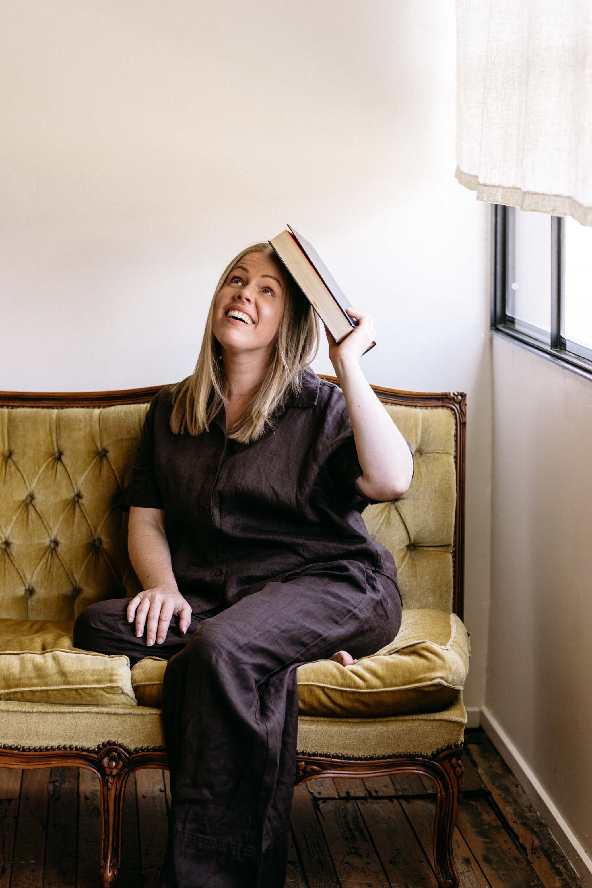 WNGSPN founder Sarah holding a book on a vintage couch, capturing a reader who feels deeply and connects through storytelling