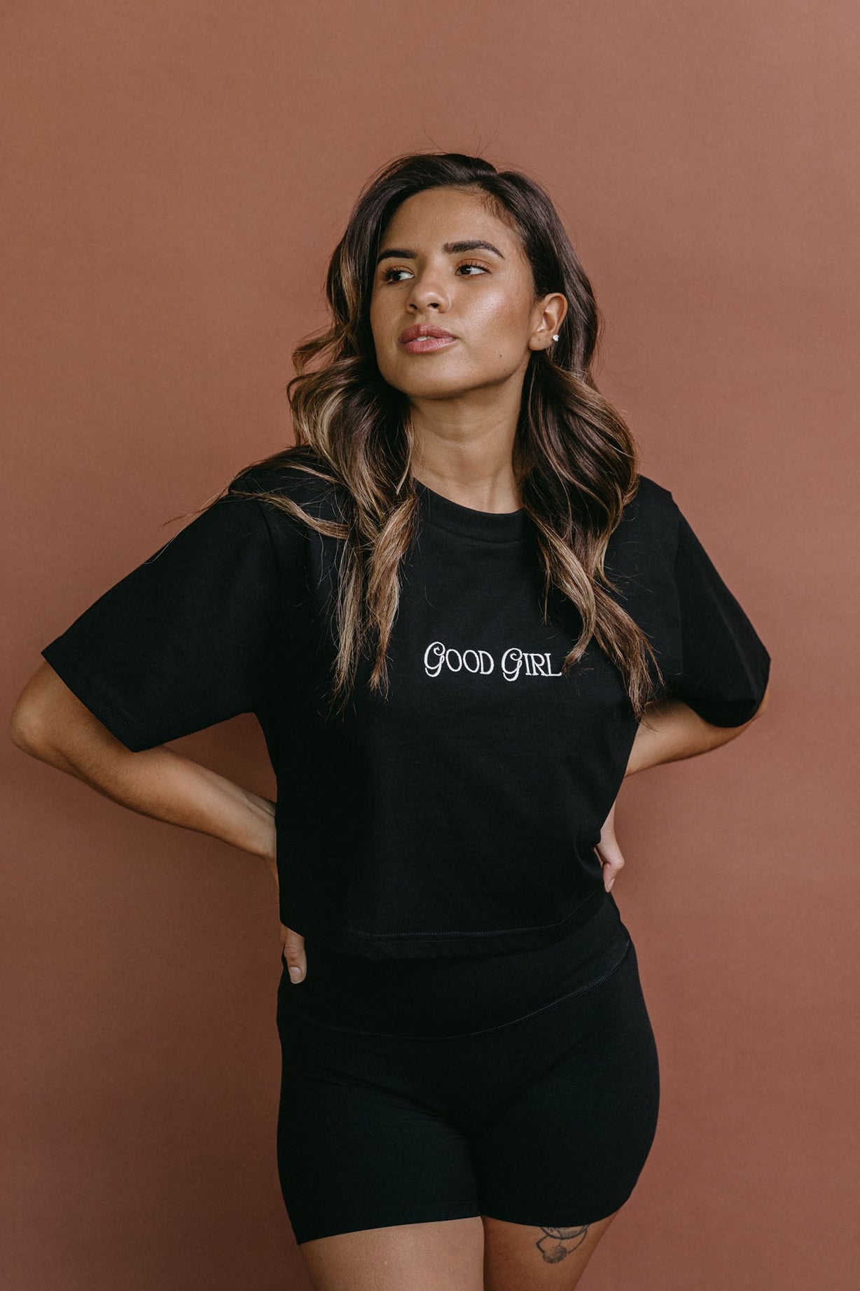 Female model wearing the black "Good Girl" cropped embroidered T-shirt by WNGSPN, styled with understated confidence.