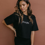 Female model wearing the black "Good Girl" cropped embroidered T-shirt by WNGSPN, styled with understated confidence.