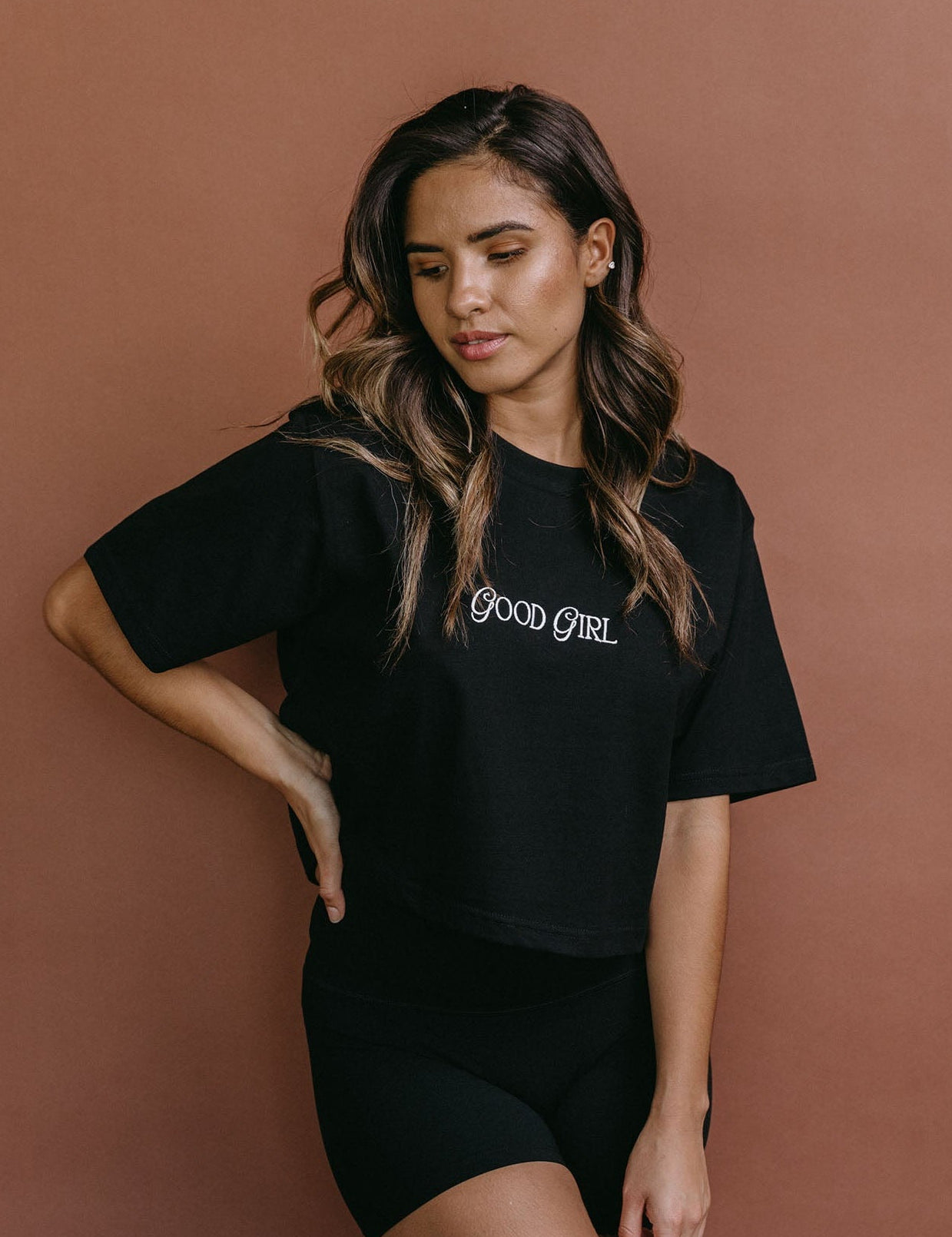 Female model wearing the black "Good Girl" cropped embroidered T-shirt by WNGSPN, styled with understated confidence.