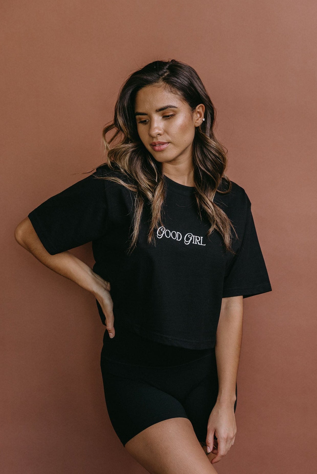 Female model wearing the black "Good Girl" cropped embroidered T-shirt by WNGSPN, styled with understated confidence.