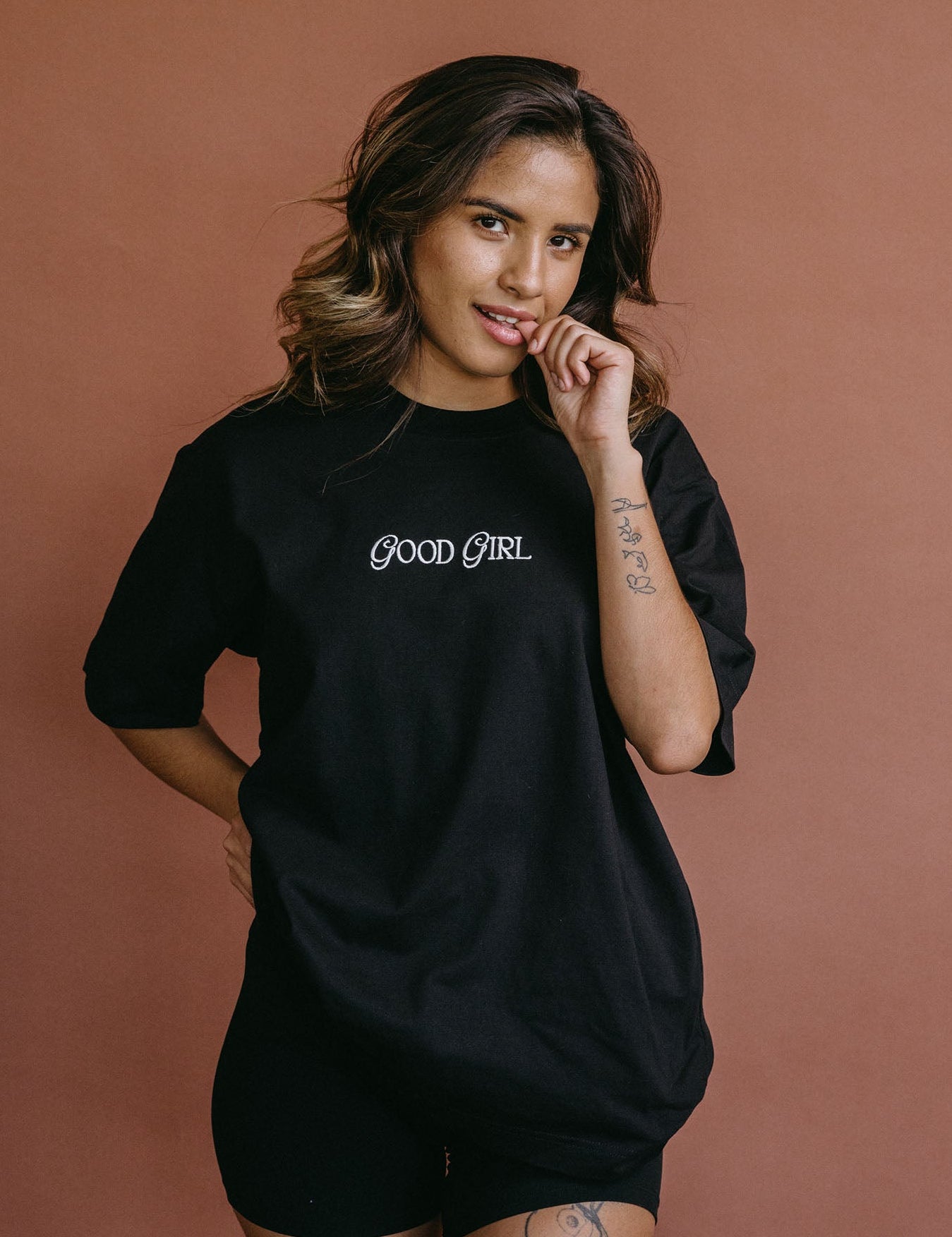 Female model wearing the black "Good Girl" relaxed fit embroidered T-shirt by WNGSPN, styled with understated confidence.