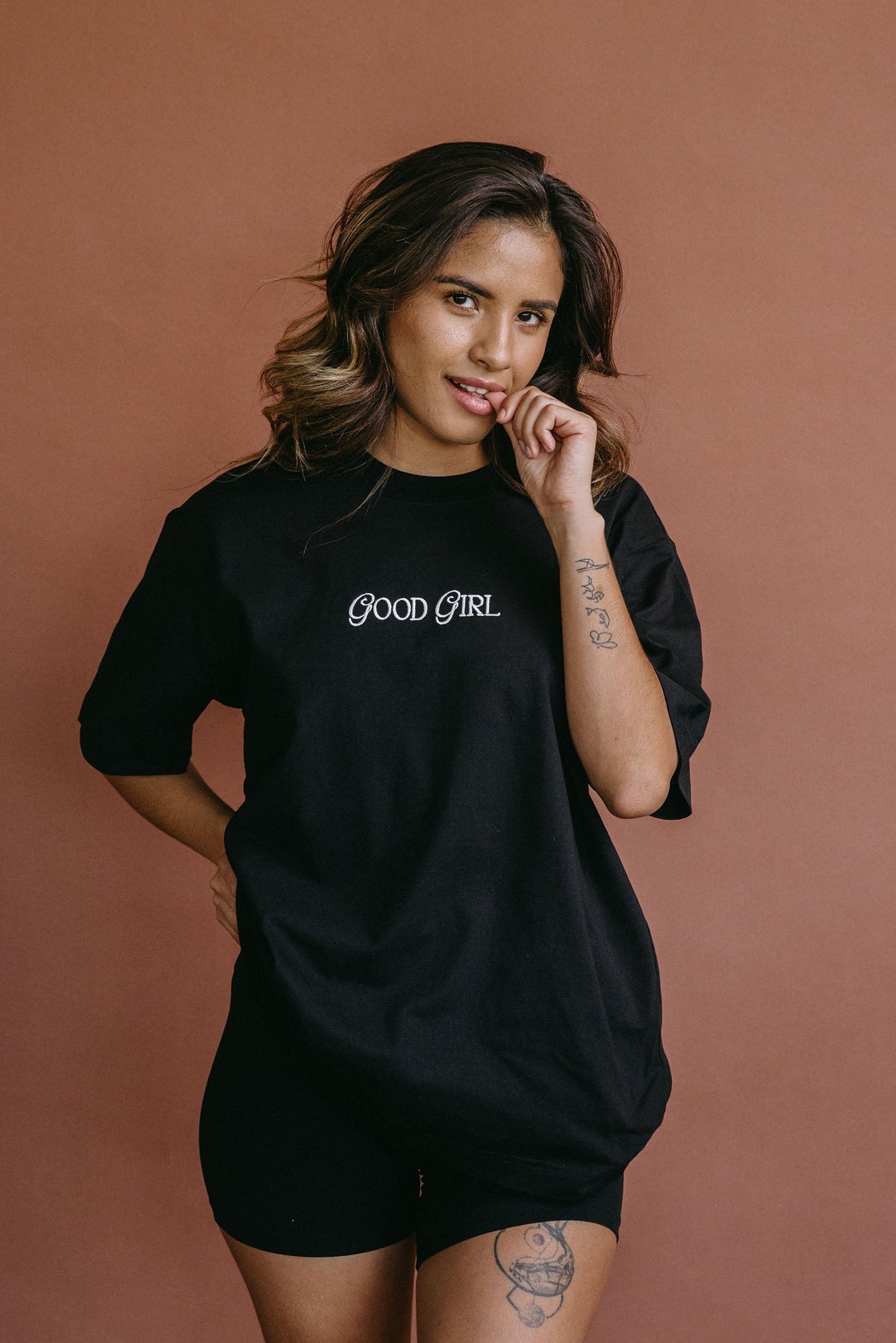 Female model wearing the black "Good Girl" relaxed fit embroidered T-shirt by WNGSPN, styled with understated confidence.