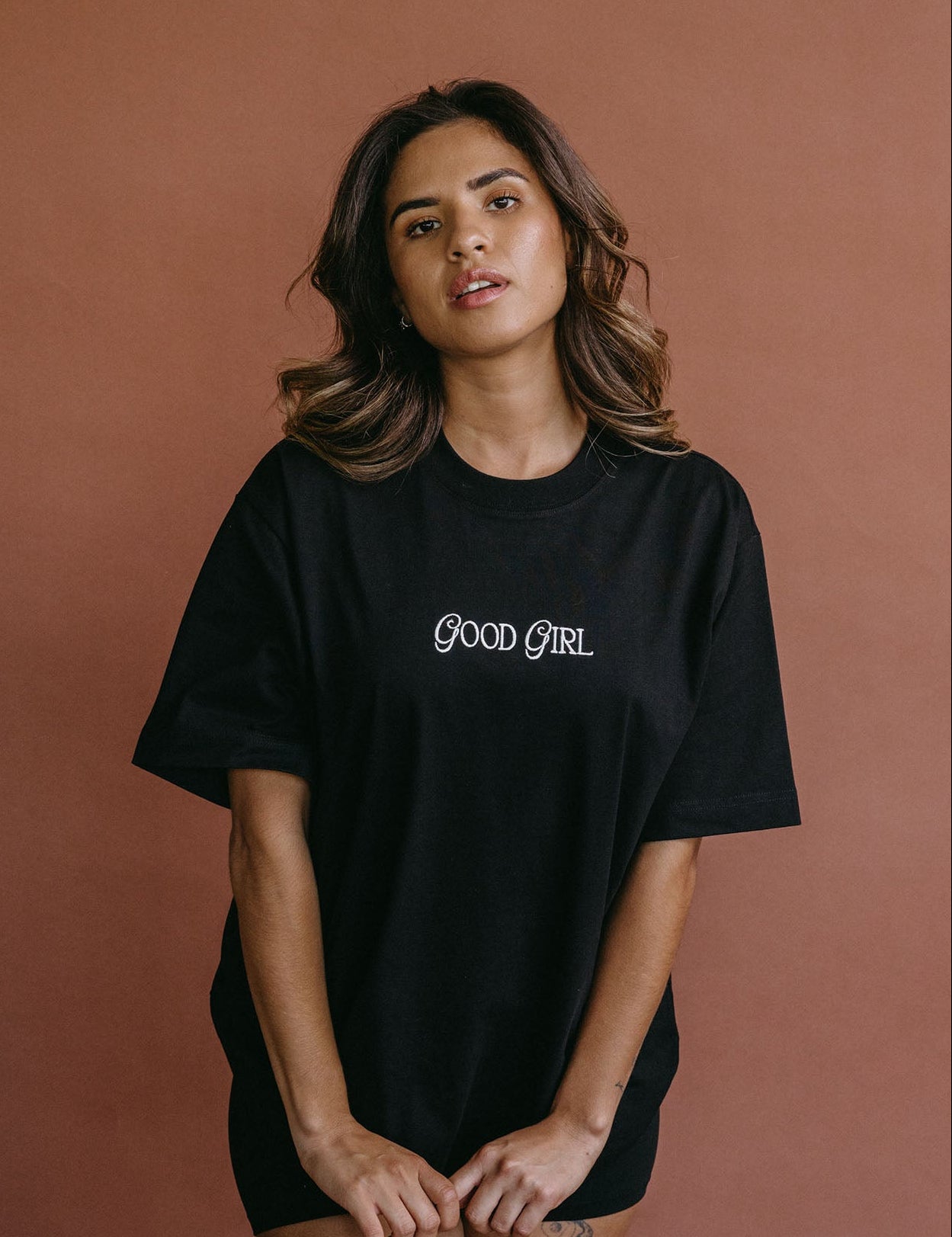 Female model wearing the black "Good Girl" relaxed fit embroidered T-shirt by WNGSPN, with a relaxed silhouette and clean lines.