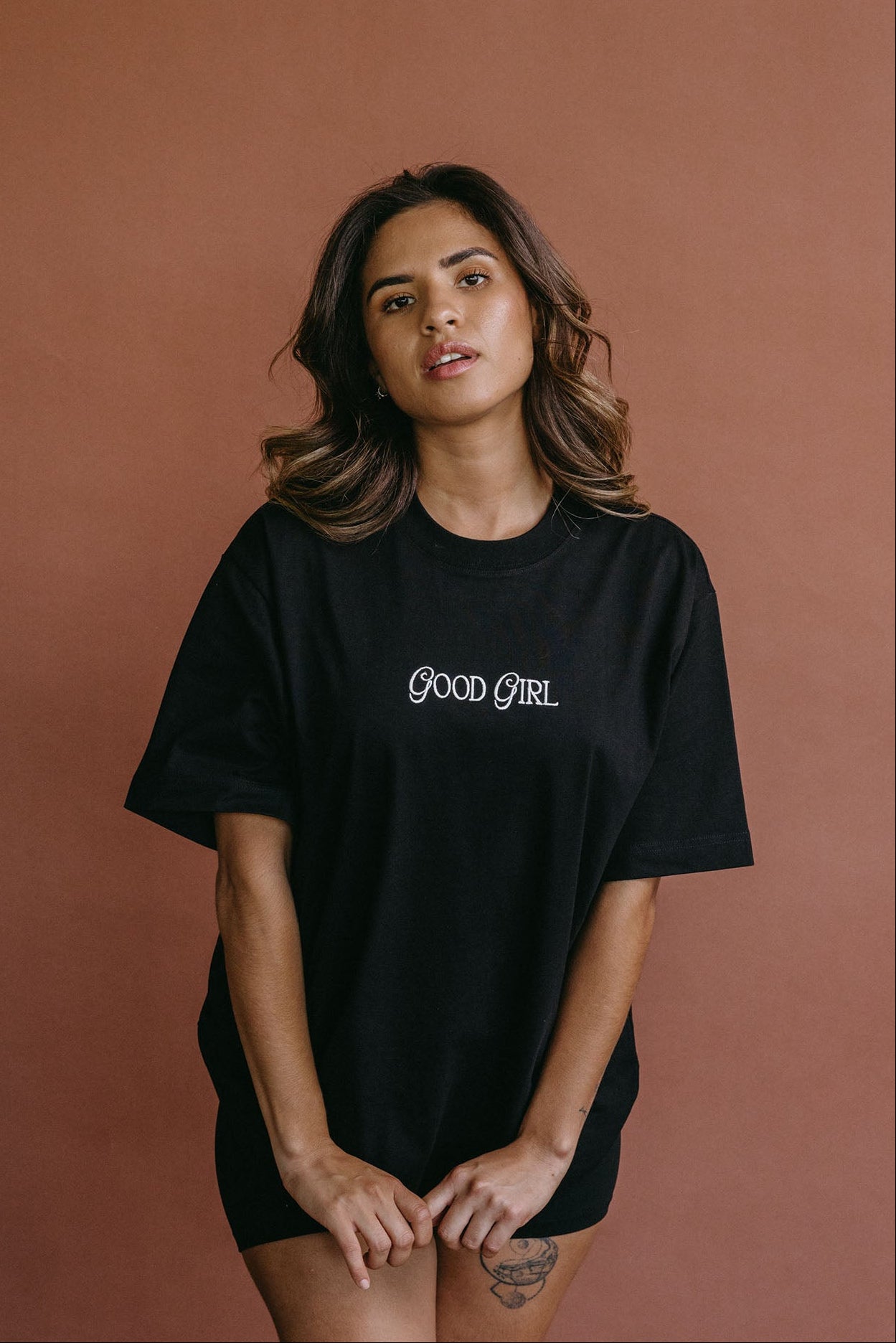 Female model wearing the black "Good Girl" relaxed fit embroidered T-shirt by WNGSPN, with a relaxed silhouette and clean lines.