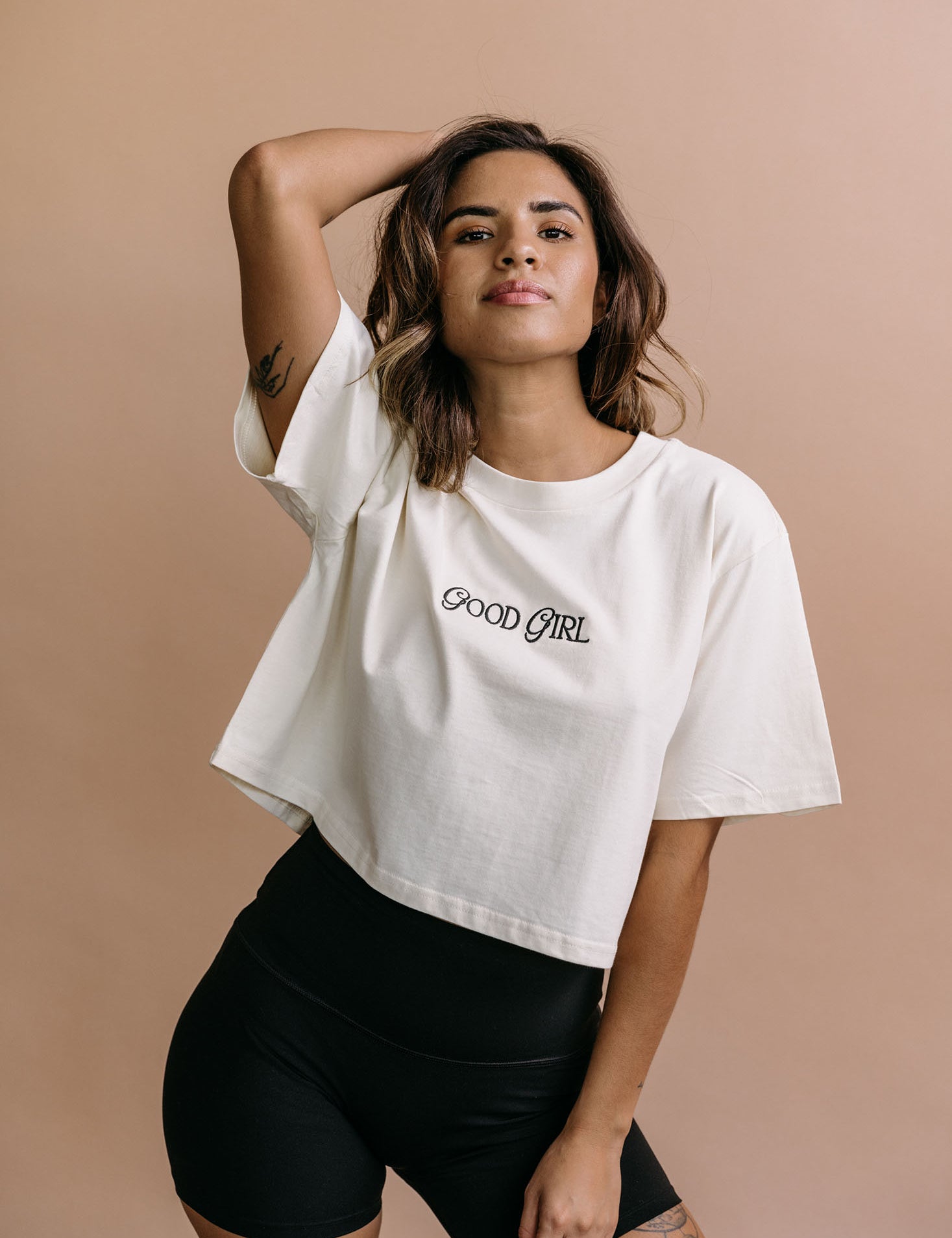 Female model wearing the ecru "Good Girl" cropped embroidered T-shirt by WNGSPN, with a relaxed silhouette and clean lines.