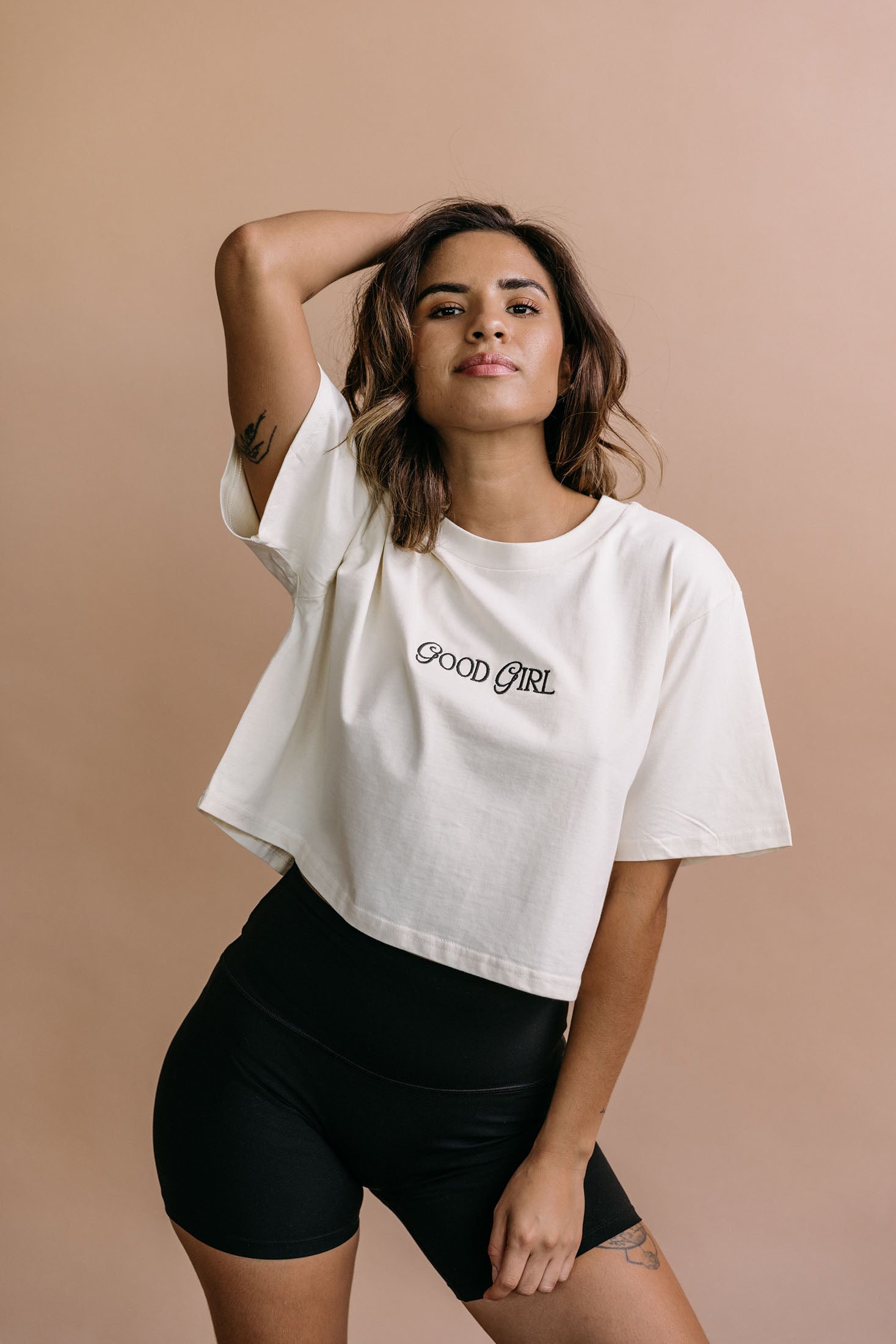 Female model wearing the ecru "Good Girl" cropped embroidered T-shirt by WNGSPN, with a relaxed silhouette and clean lines.