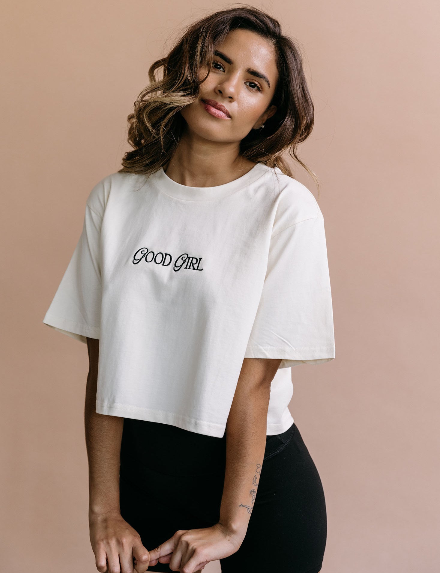 Female model wearing the ecru "Good Girl" cropped embroidered T-shirt by WNGSPN, with a relaxed silhouette and clean lines.