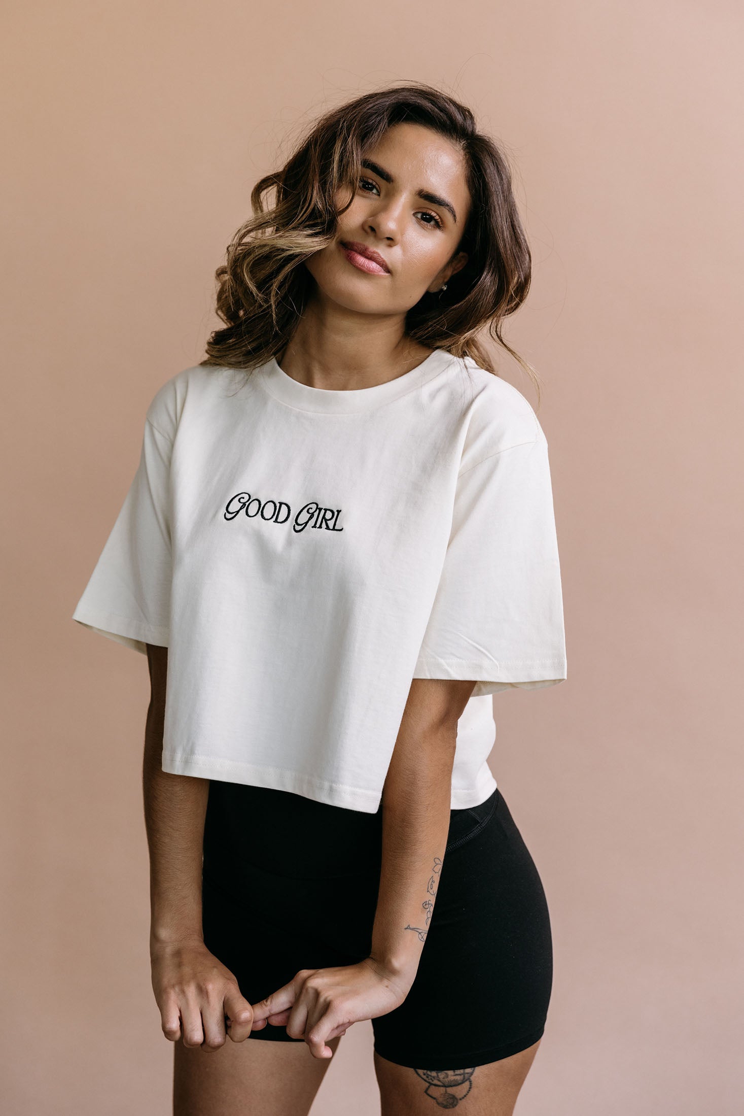 Female model wearing the ecru "Good Girl" cropped embroidered T-shirt by WNGSPN, with a relaxed silhouette and clean lines.