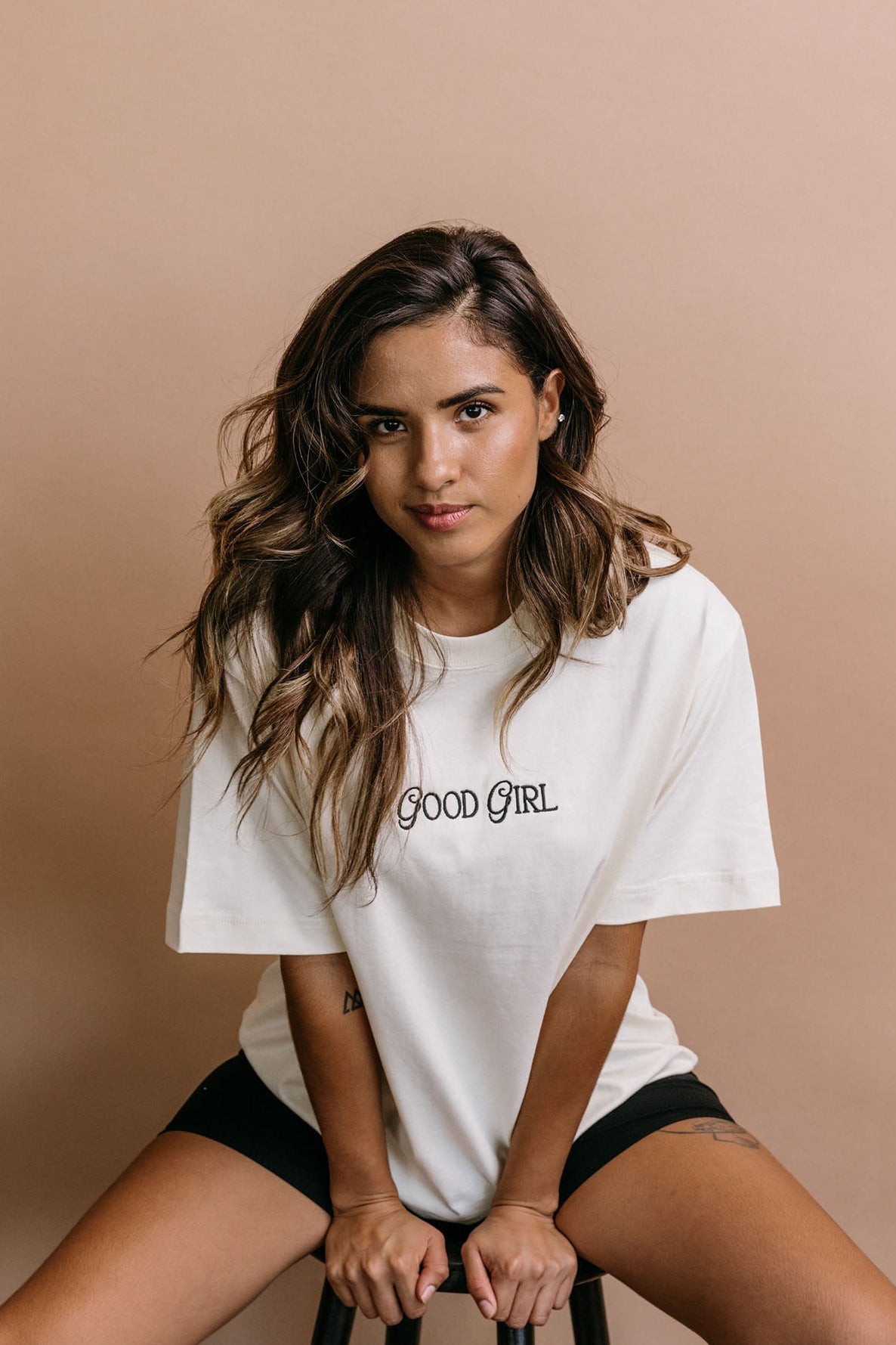 Female model wearing the ecru "Good Girl" relaxed fit embroidered T-shirt by WNGSPN, styled with understated confidence.