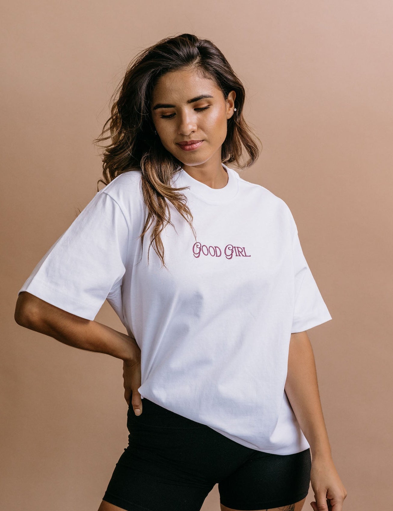 Female model wearing the white "Good Girl" relaxed fit embroidered T-shirt by WNGSPN, styled in a minimal, elevated aesthetic.