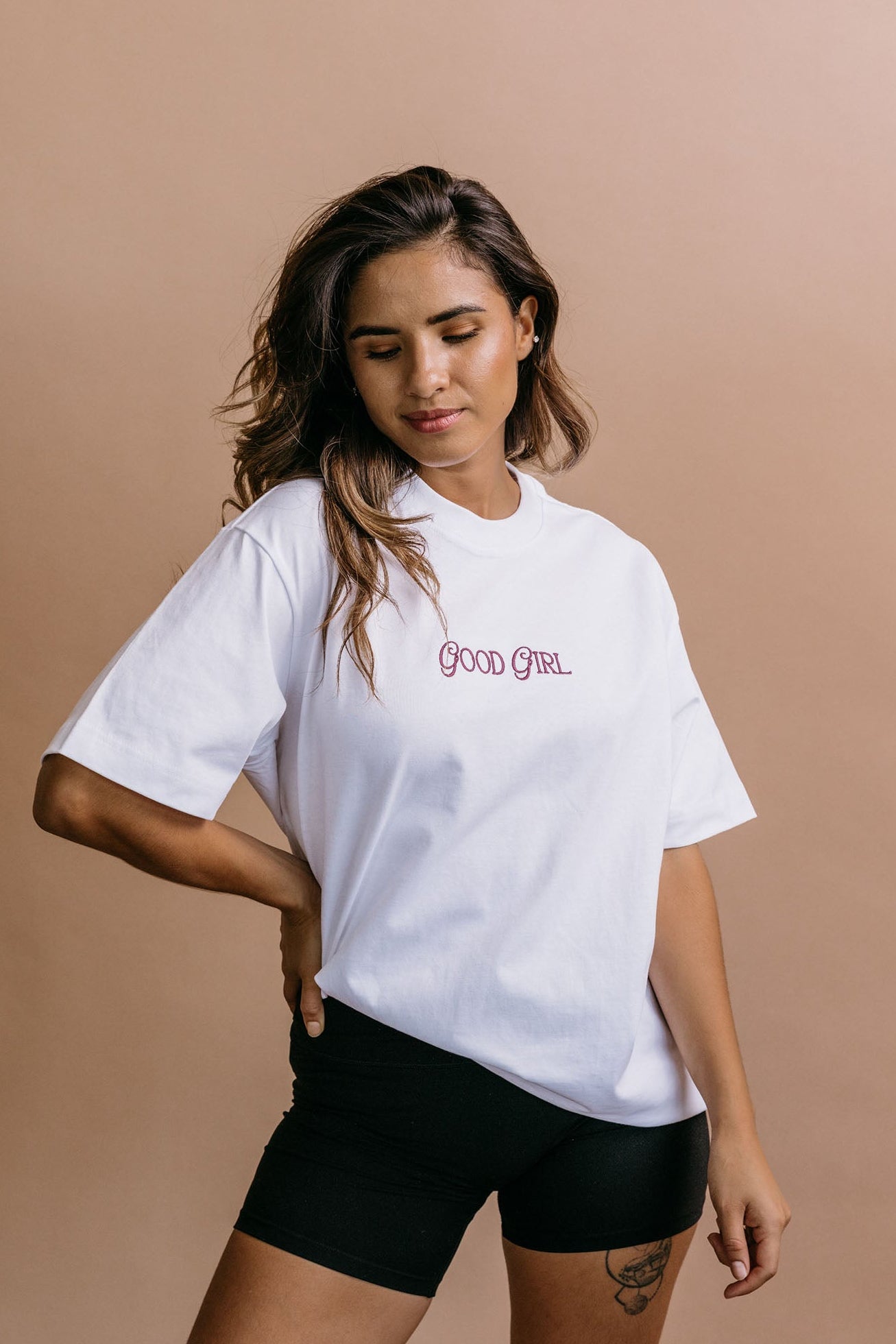 Female model wearing the white "Good Girl" relaxed fit embroidered T-shirt by WNGSPN, styled in a minimal, elevated aesthetic.