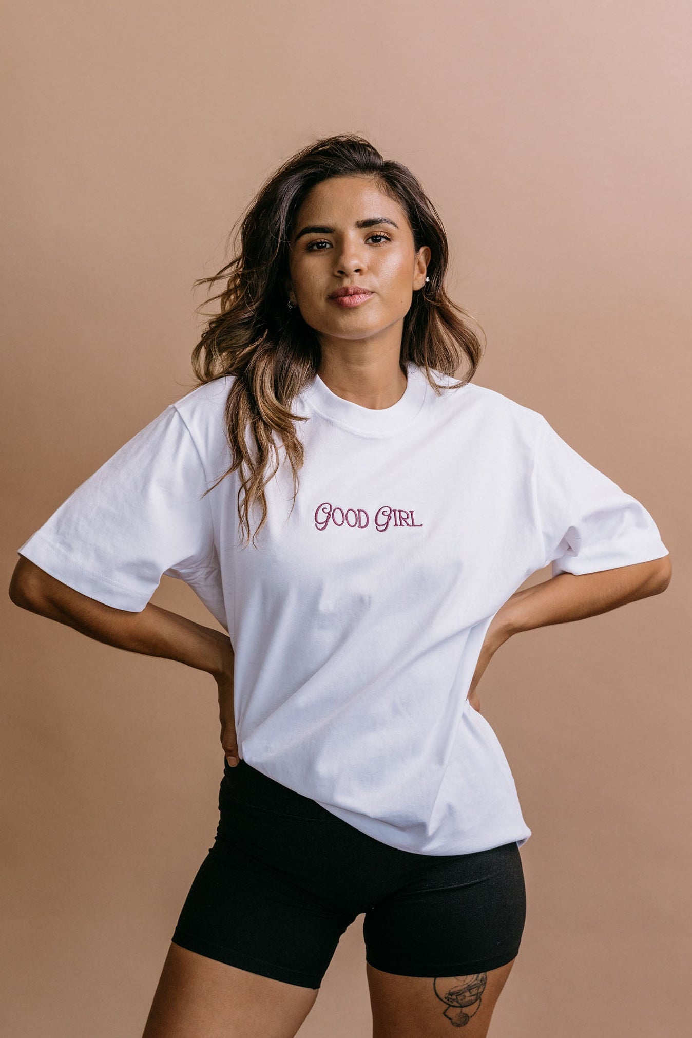 Female model wearing the white "Good Girl" relaxed fit embroidered T-shirt by WNGSPN, with a relaxed silhouette and clean lines.