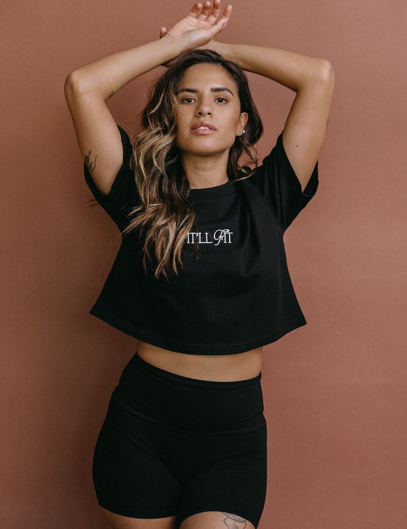 Female model wearing the black "It'll Fit" cropped embroidered T-shirt by WNGSPN, styled with understated confidence.