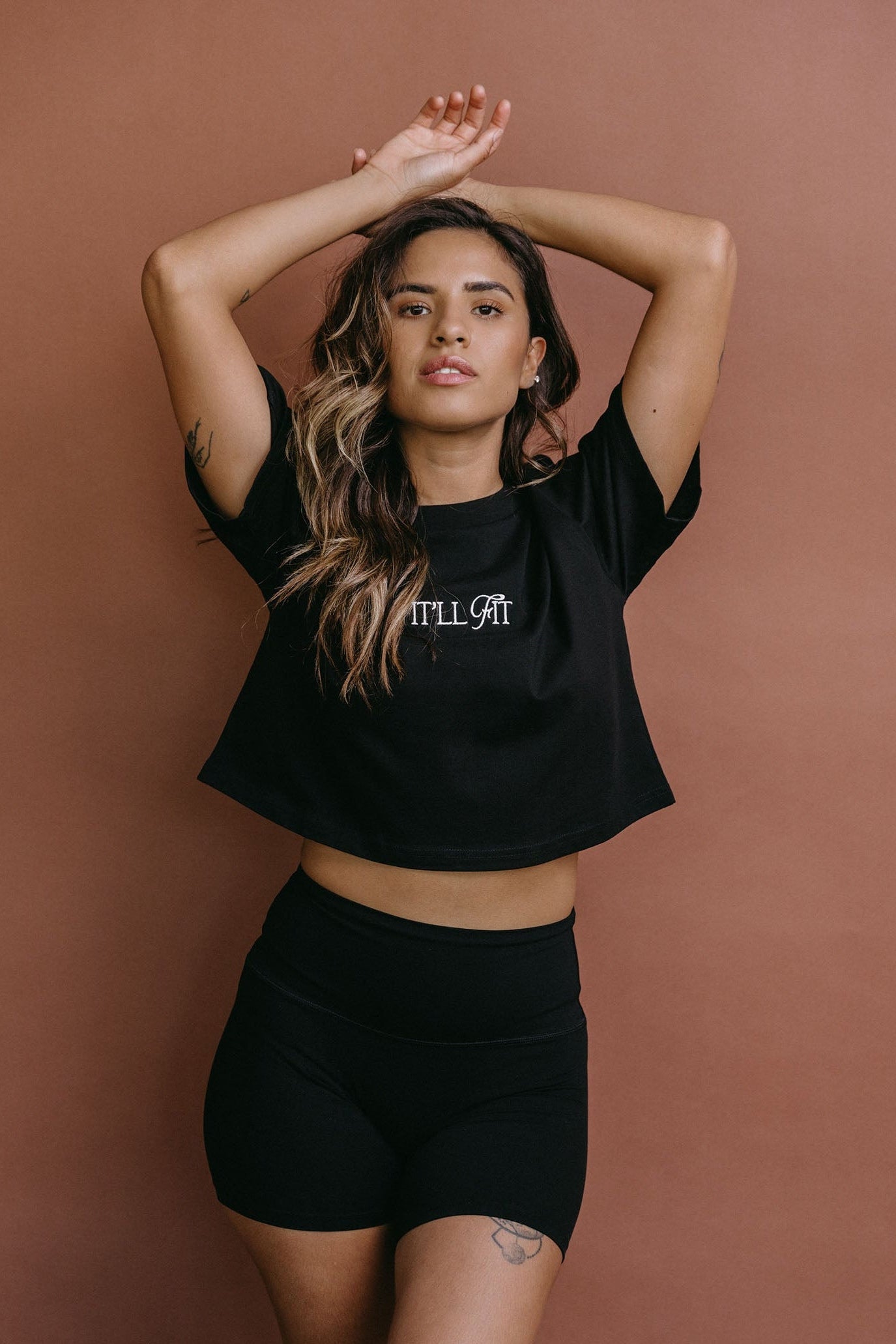 Female model wearing the black "It'll Fit" cropped embroidered T-shirt by WNGSPN, styled with understated confidence.