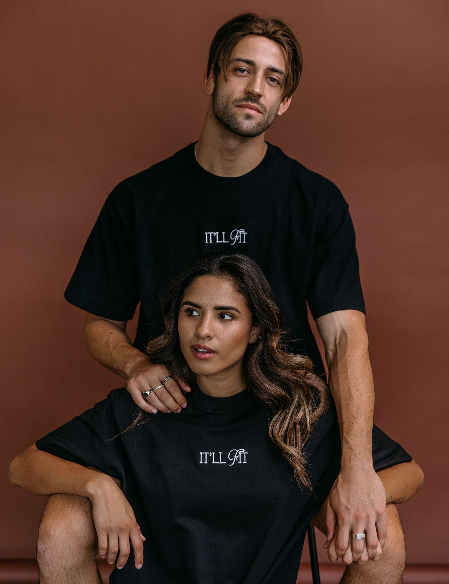 Couple wearing the black "It'll Fit" relaxed fit embroidered T-shirt by WNGSPN, styled as elevated romance reader apparel.