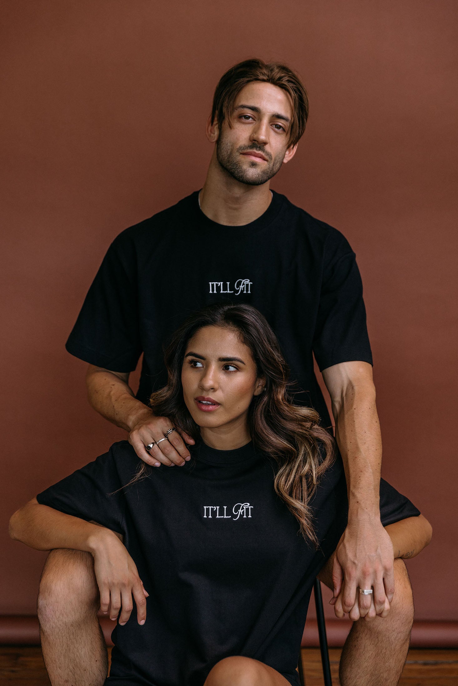 Couple wearing the black "It'll Fit" relaxed fit embroidered T-shirt by WNGSPN, styled as elevated romance reader apparel.