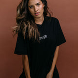 Female model wearing the black "It'll Fit" relaxed fit embroidered T-shirt by WNGSPN, styled with understated confidence.