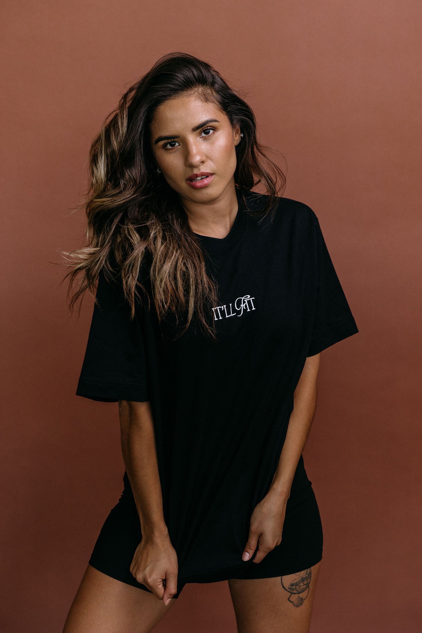 Female model wearing the black "It'll Fit" relaxed fit embroidered T-shirt by WNGSPN, styled with understated confidence.