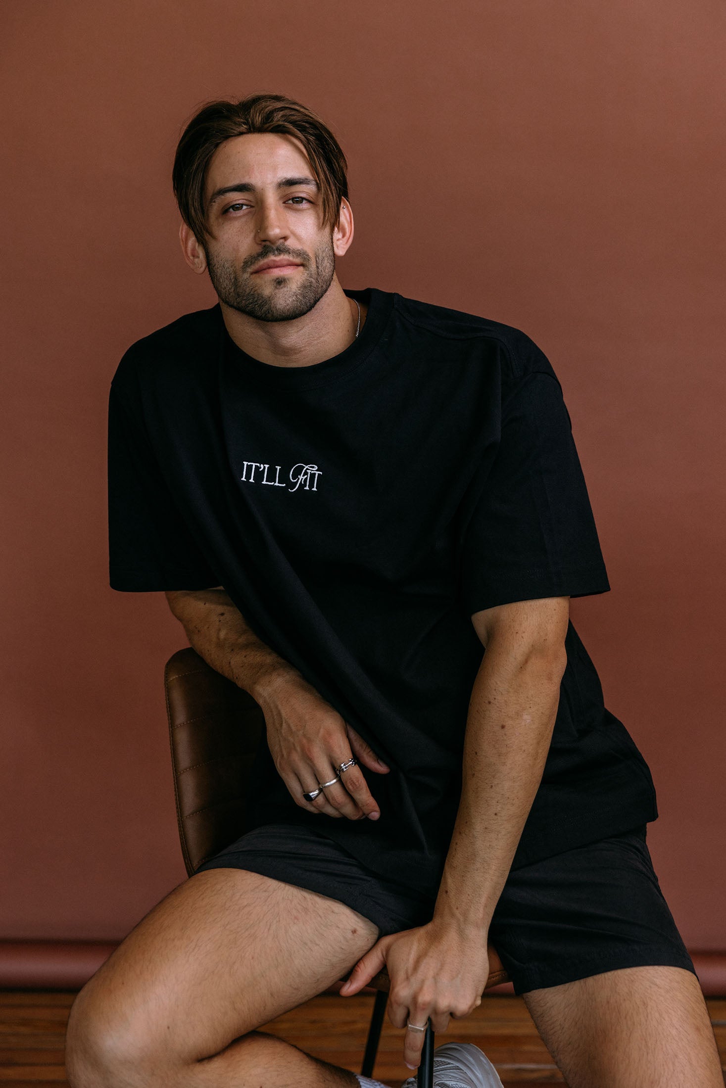 Male model wearing the black "It'll Fit" relaxed fit embroidered T-shirt by WNGSPN, styled with understated confidence.