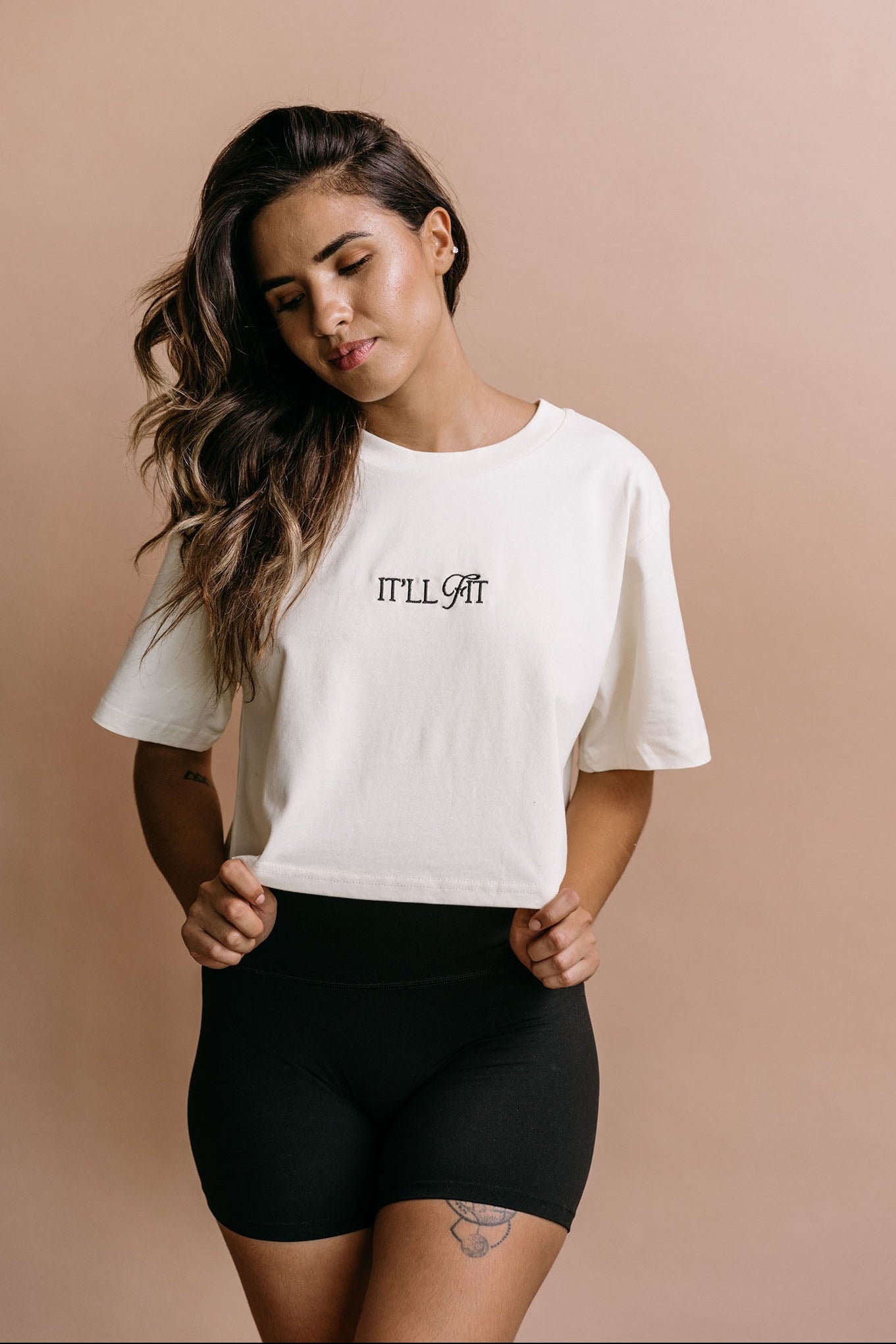 Female model wearing the ecru "It'll Fit" cropped embroidered T-shirt by WNGSPN, with a relaxed silhouette and clean lines.