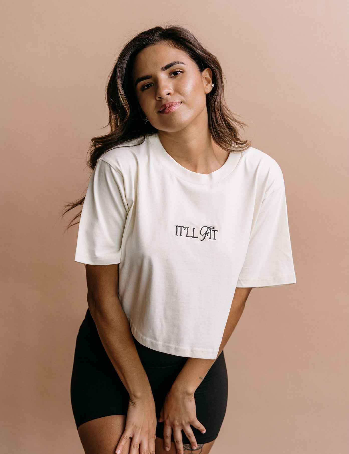 Female model wearing the ecru "It'll Fit" cropped embroidered T-shirt by WNGSPN, with a relaxed silhouette and clean lines.