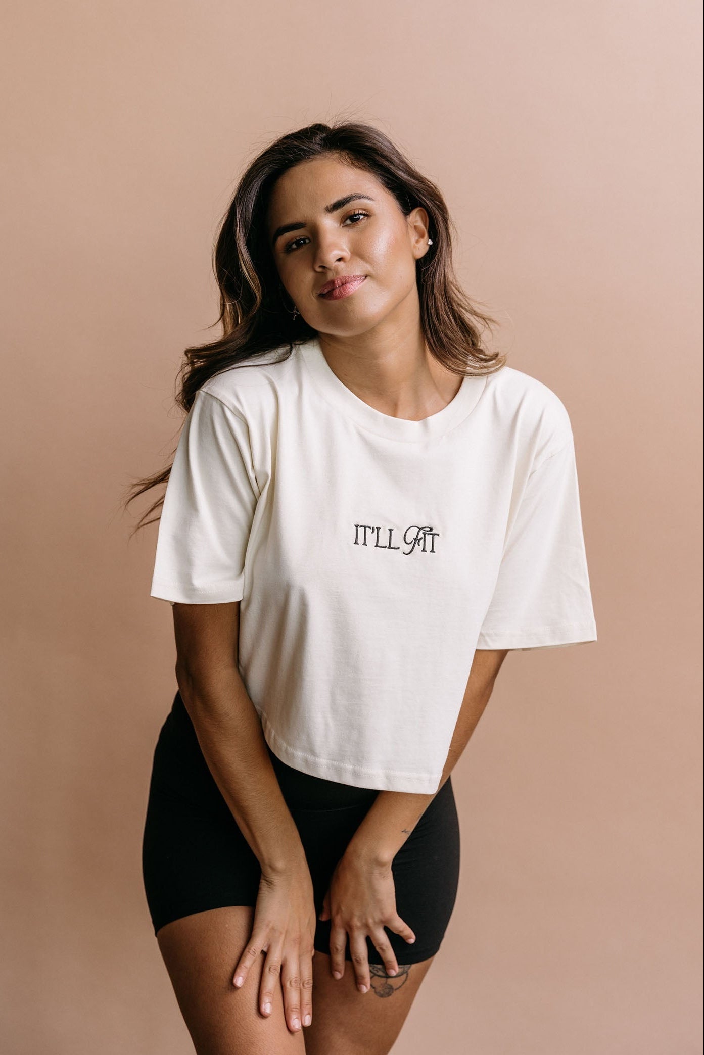 Female model wearing the ecru "It'll Fit" cropped embroidered T-shirt by WNGSPN, with a relaxed silhouette and clean lines.