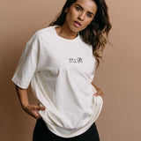 Female model wearing the ecru "It'll Fit" relaxed fit embroidered T-shirt by WNGSPN, styled in a minimal, elevated aesthetic.