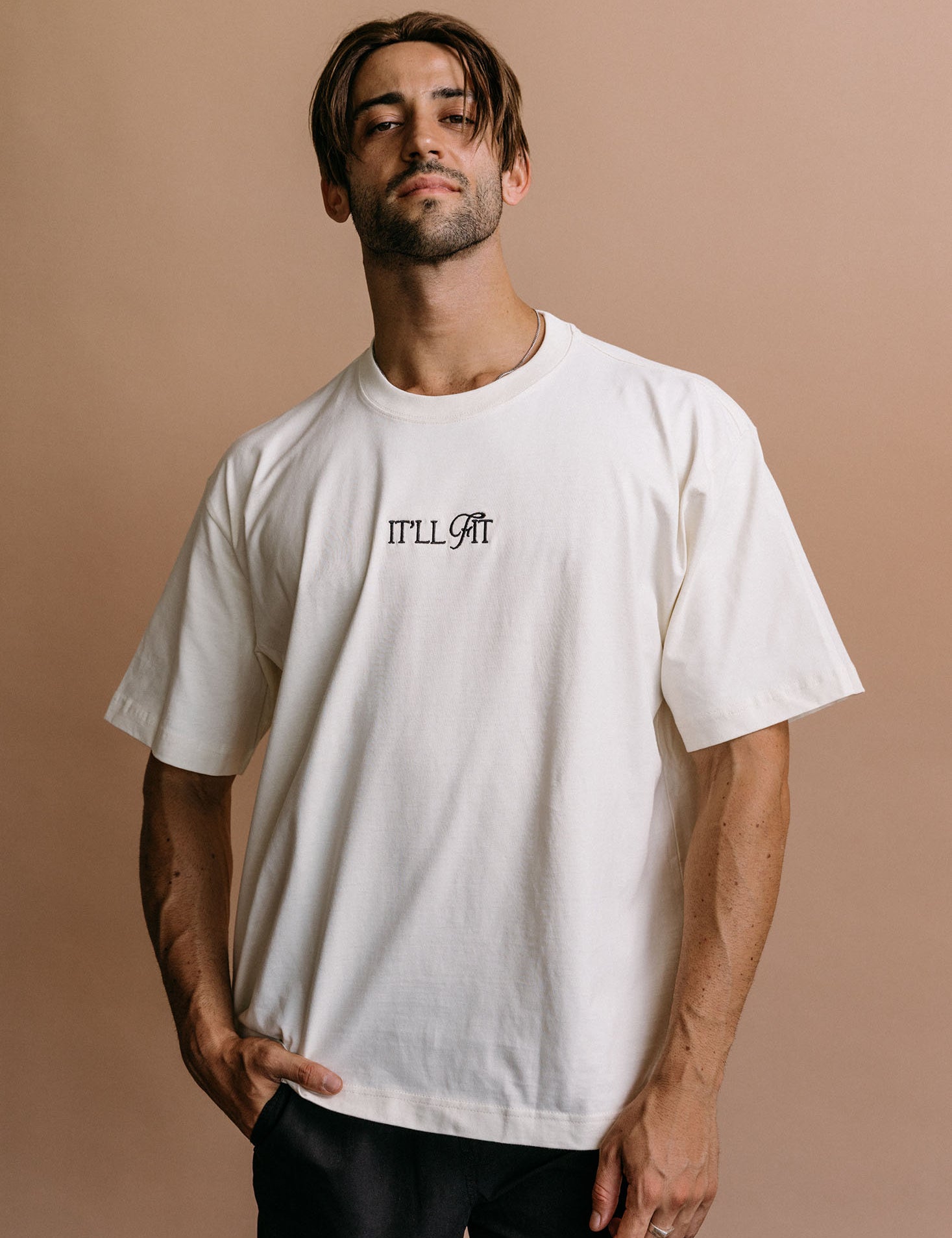 Male model wearing the ecru "It'll Fit" relaxed fit embroidered T-shirt by WNGSPN, styled in a minimal, elevated aesthetic.