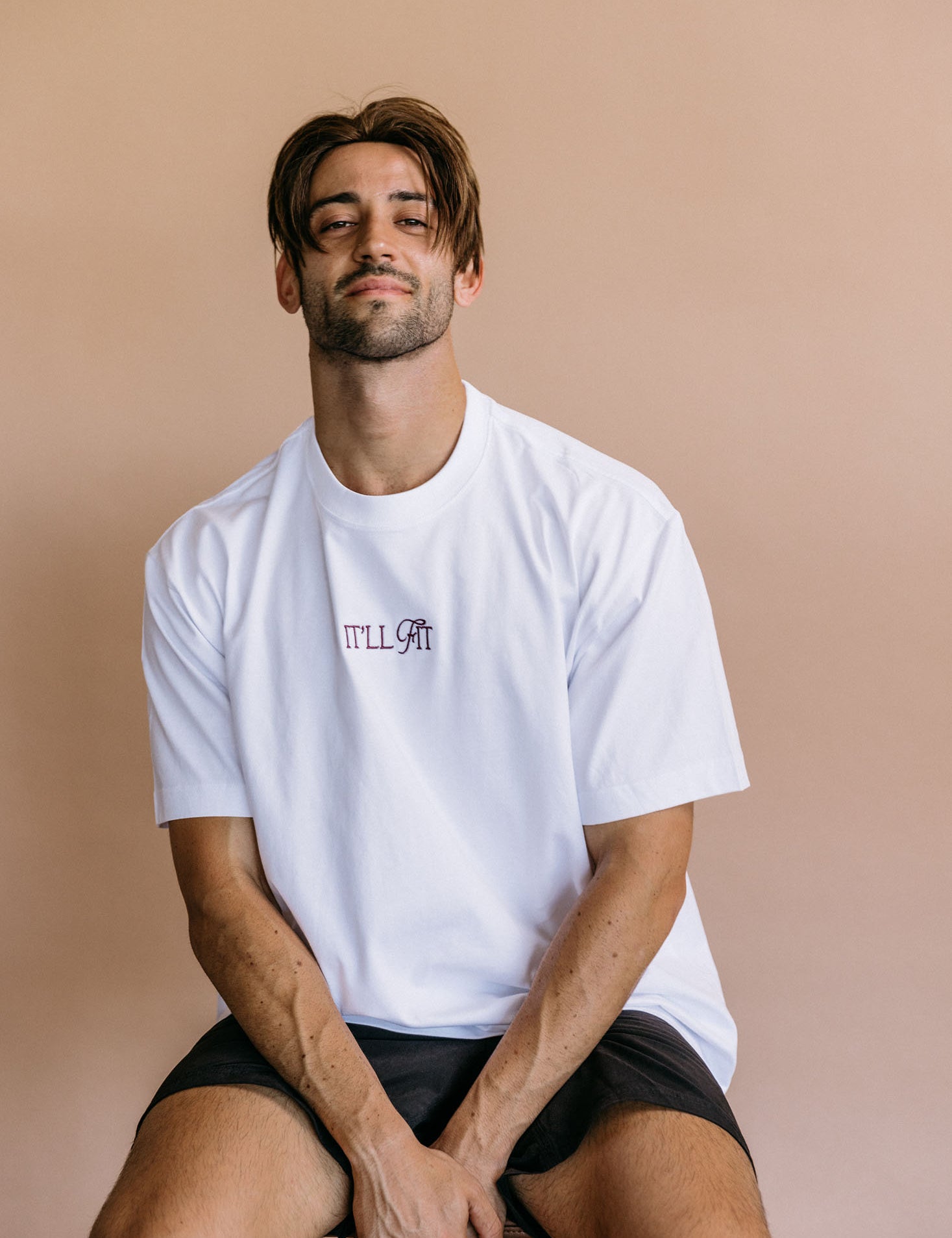 Female model wearing the white "It'll Fit" relaxed fit embroidered T-shirt by WNGSPN, with a relaxed silhouette and clean lines.