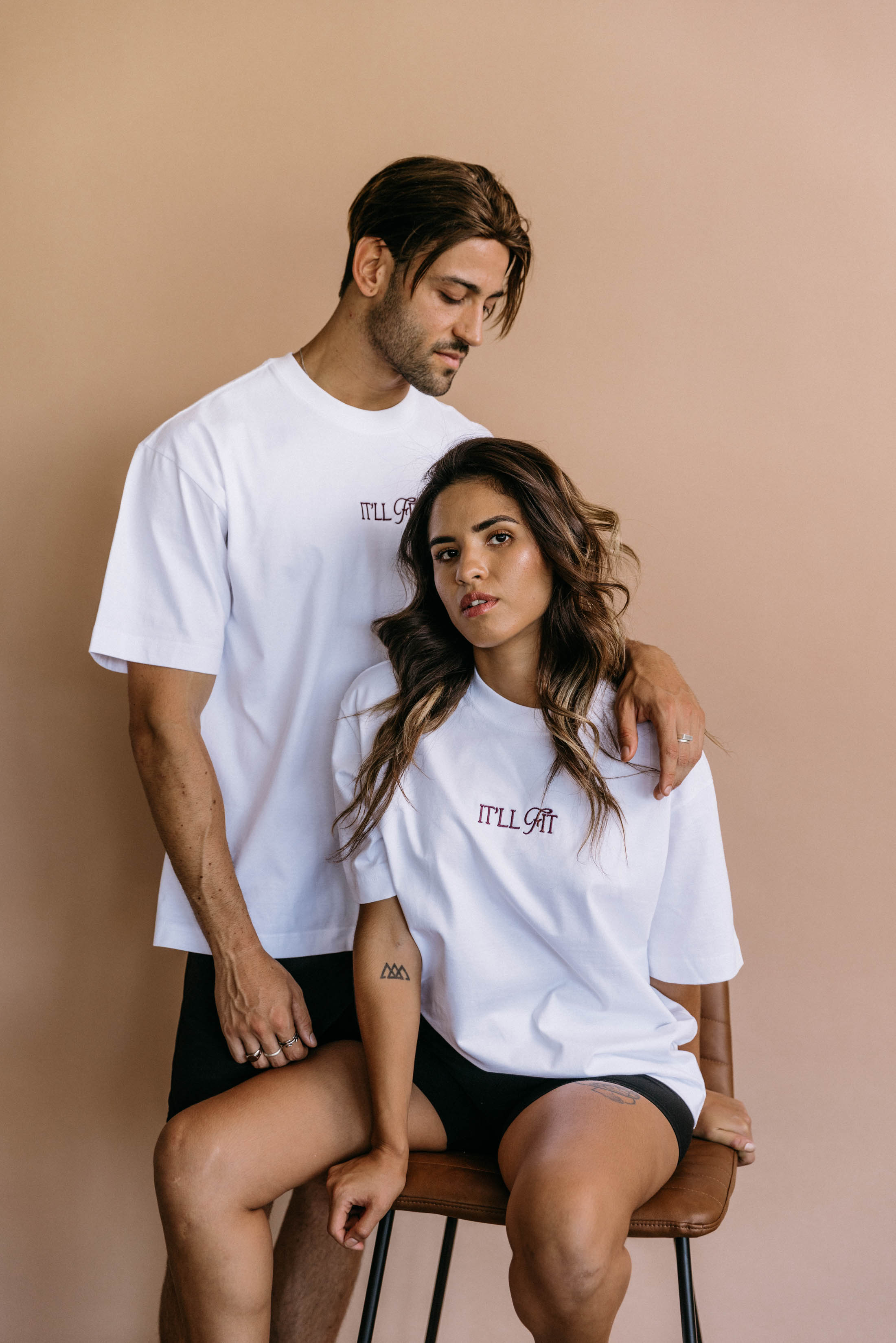 Couple wearing the white "It'll Fit" relaxed fit embroidered T-shirt by WNGSPN, with subtle tension and modern edge.