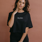 Female model wearing the black "Oh Gods" cropped embroidered T-shirt by WNGSPN, styled with understated confidence.