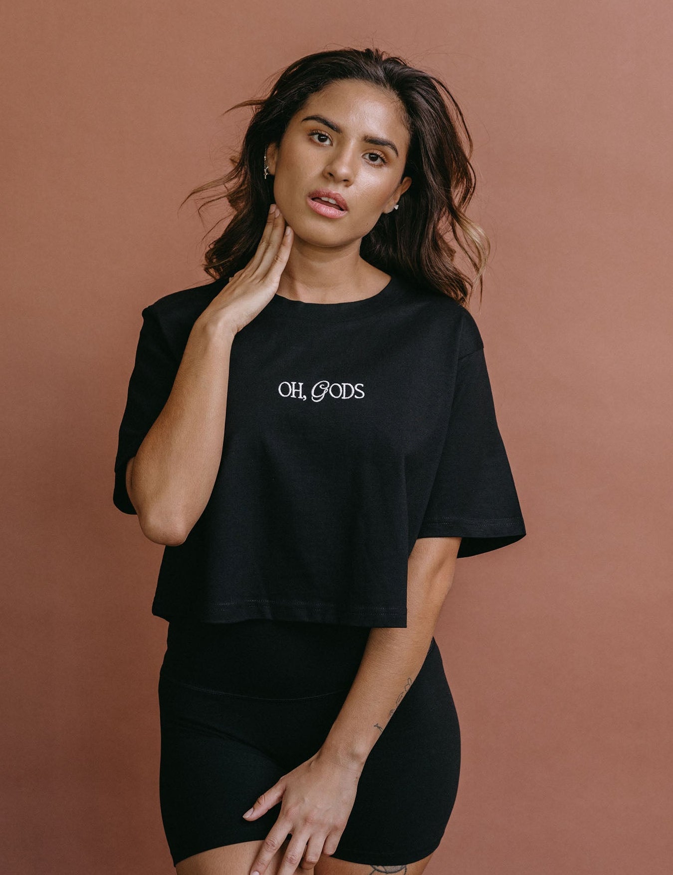 Female model wearing the black "Oh Gods" cropped embroidered T-shirt by WNGSPN, styled with understated confidence.