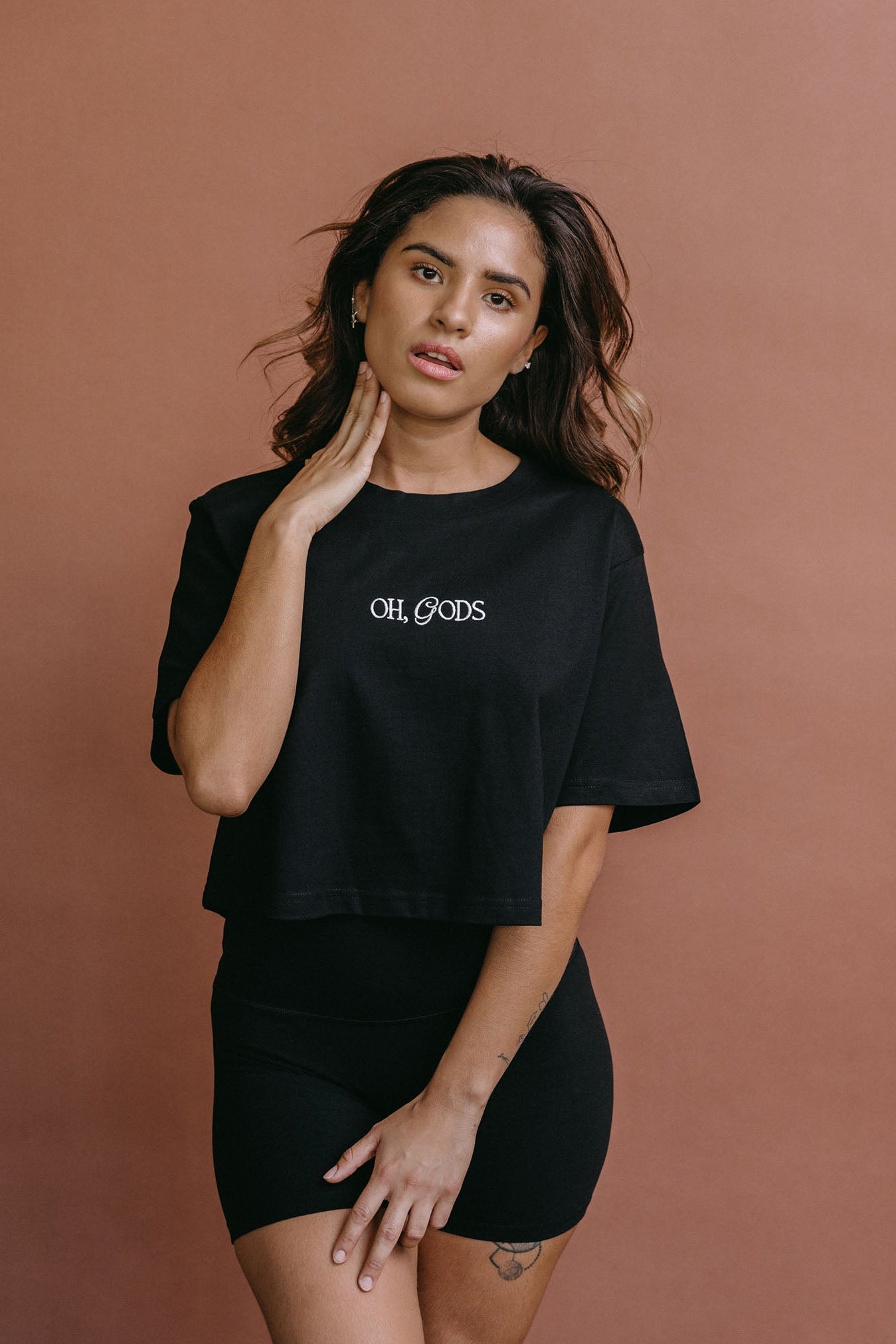 Female model wearing the black "Oh Gods" cropped embroidered T-shirt by WNGSPN, styled with understated confidence.