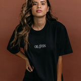 Female model wearing the black "Oh Gods" relaxed fit embroidered T-shirt by WNGSPN, styled with understated confidence.