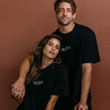 Couple wearing the black "Oh Gods" relaxed fit embroidered T-shirt by WNGSPN, styled as elevated romance reader apparel.