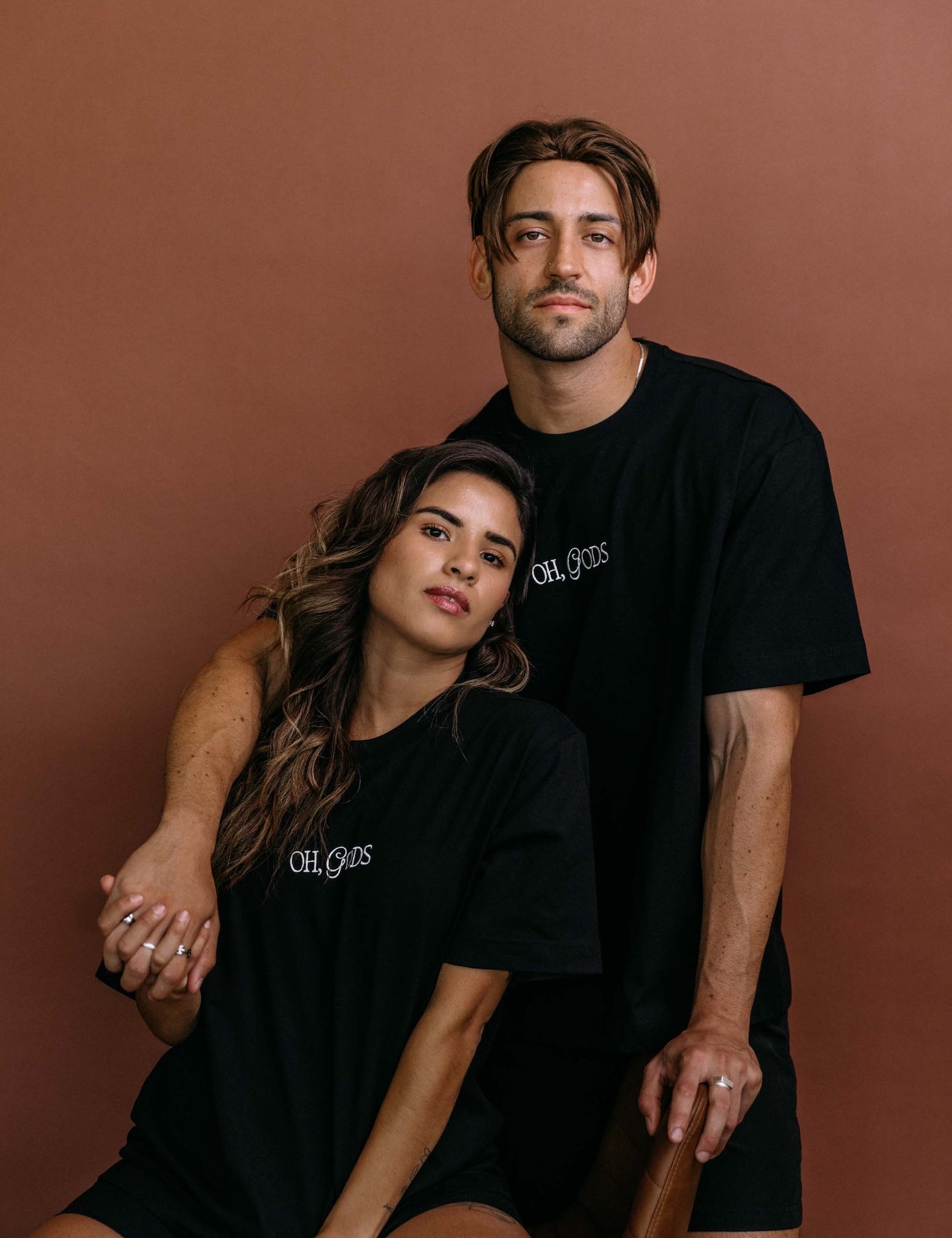 Couple wearing the black "Oh Gods" relaxed fit embroidered T-shirt by WNGSPN, styled as elevated romance reader apparel.