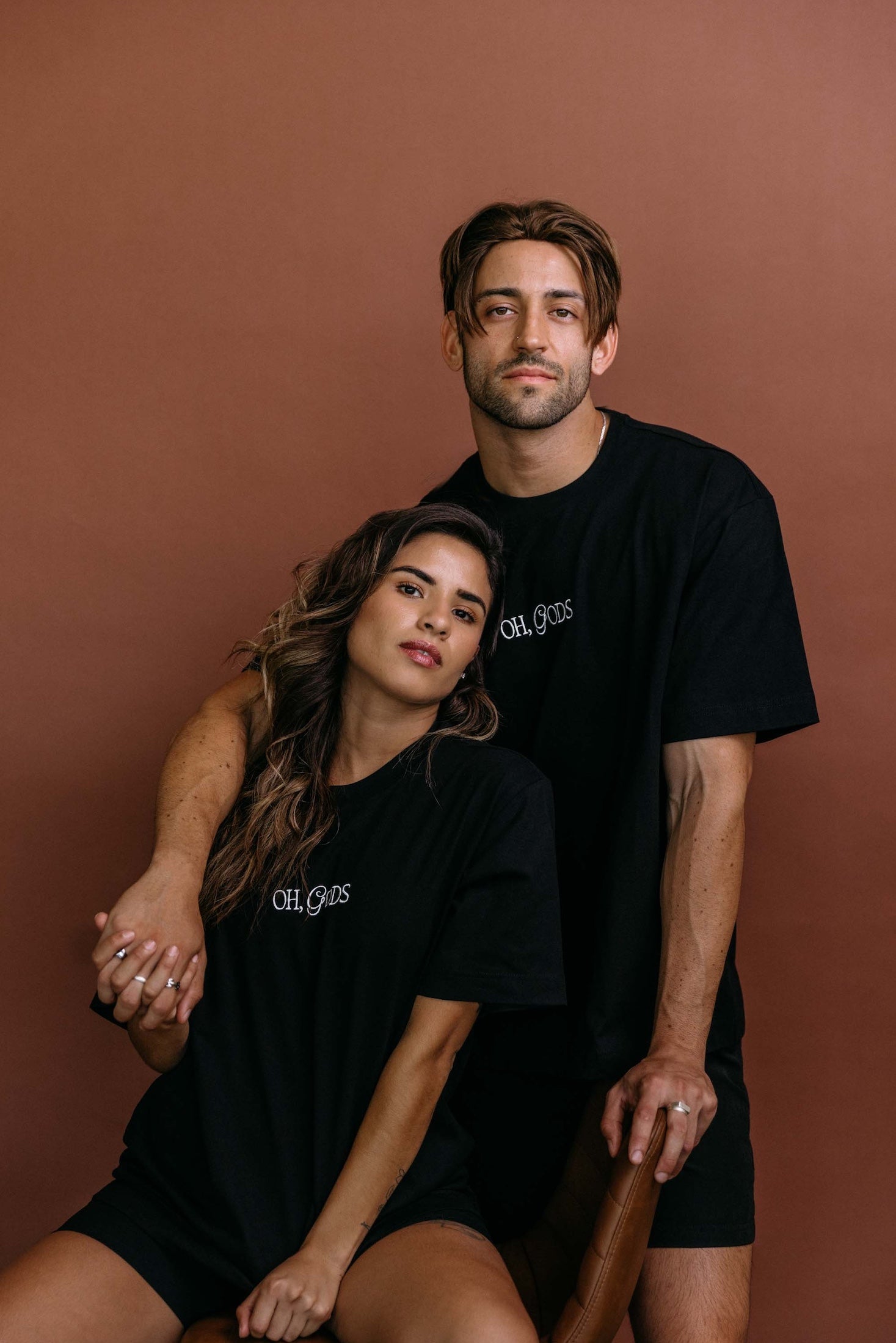 Couple wearing the black "Oh Gods" relaxed fit embroidered T-shirt by WNGSPN, styled as elevated romance reader apparel.
