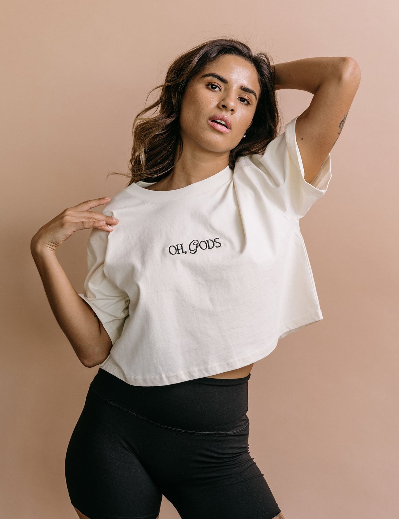 Female model wearing the ecru "Oh Gods" cropped embroidered T-shirt by WNGSPN, with a relaxed silhouette and clean lines.