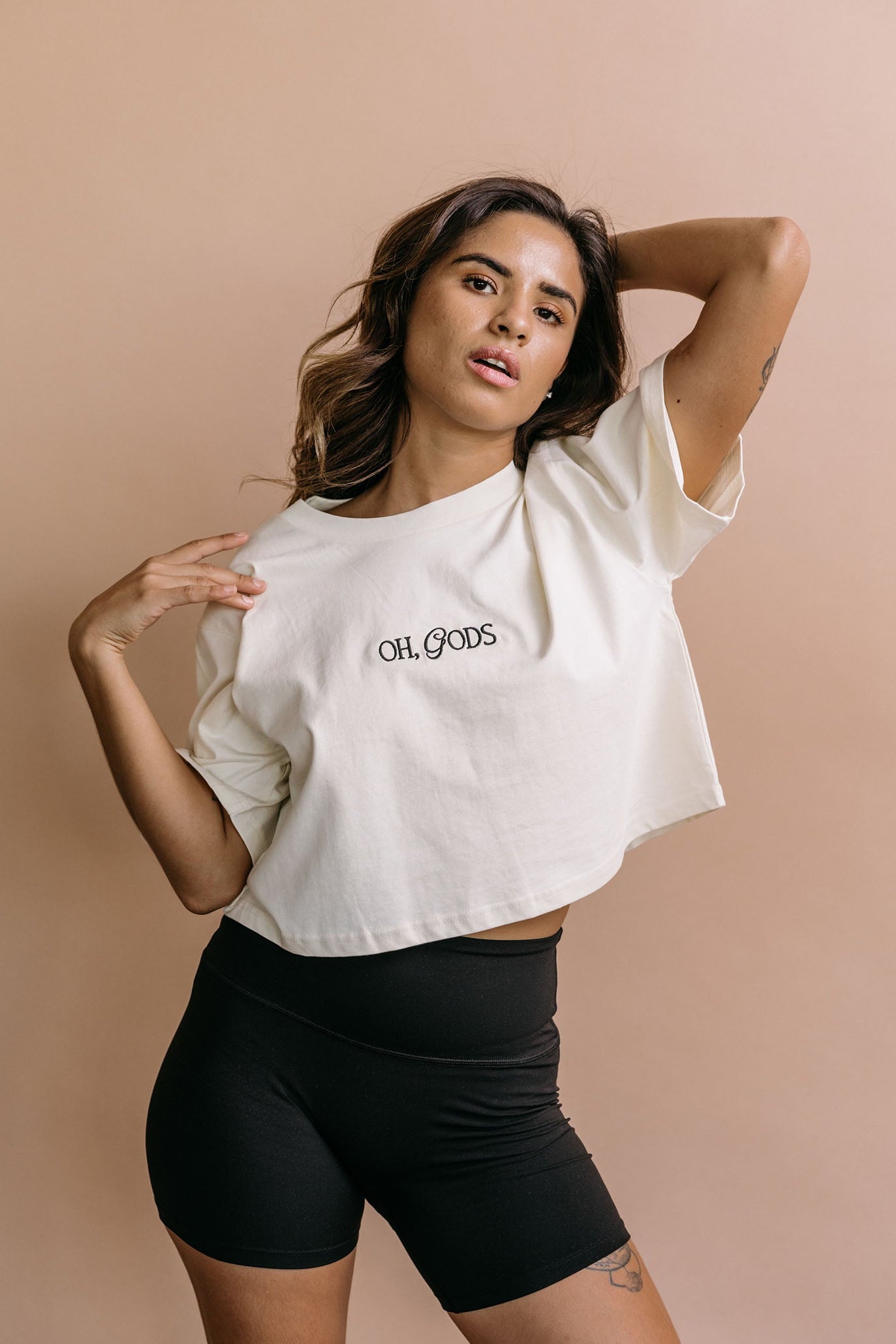 Female model wearing the ecru "Oh Gods" cropped embroidered T-shirt by WNGSPN, with a relaxed silhouette and clean lines.