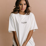 Female model wearing the ecru "Oh Gods" relaxed fit embroidered T-shirt by WNGSPN, styled in a minimal, elevated aesthetic.