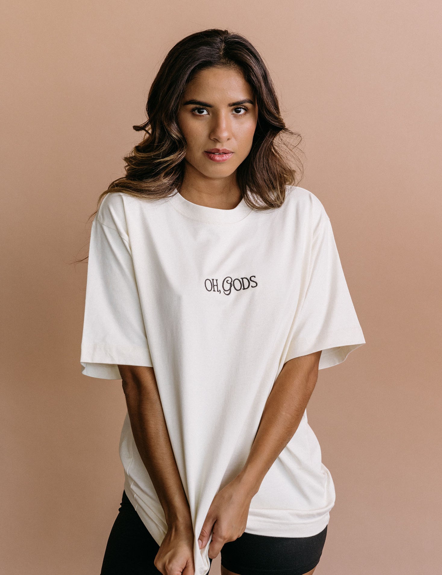 Female model wearing the ecru "Oh Gods" relaxed fit embroidered T-shirt by WNGSPN, styled in a minimal, elevated aesthetic.