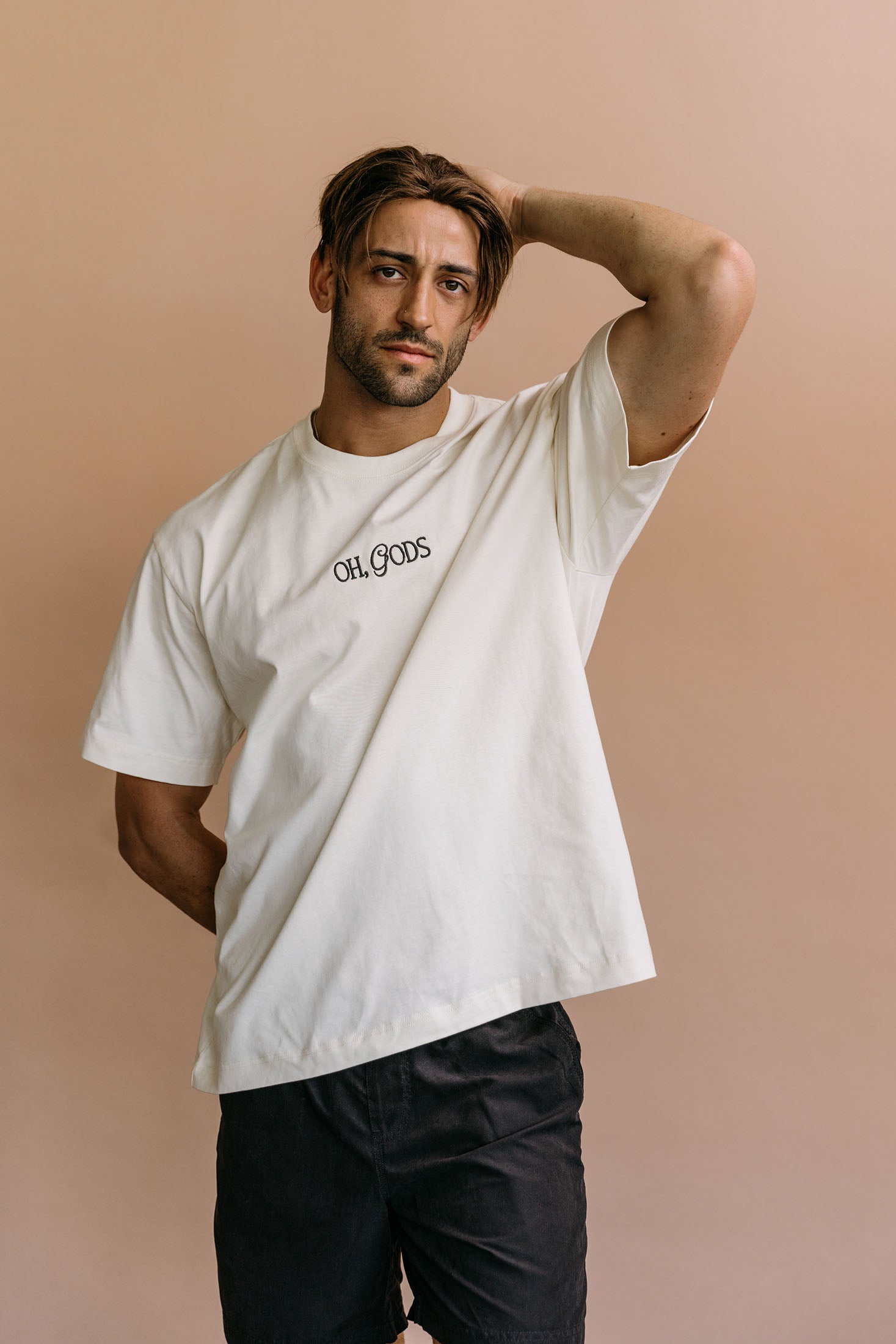 Male model wearing the ecru "Oh Gods" relaxed fit embroidered T-shirt by WNGSPN, styled in a minimal, elevated aesthetic.