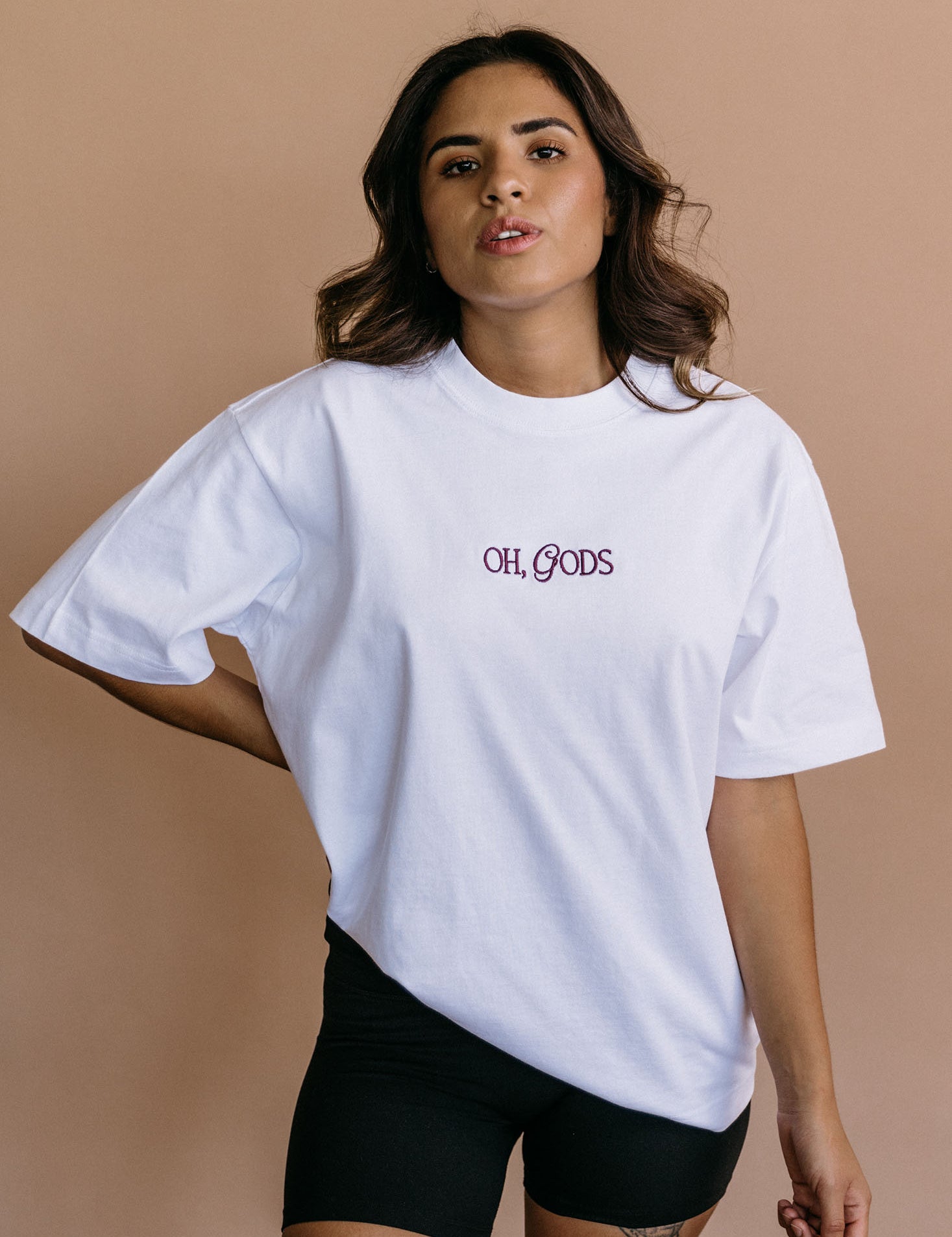 Female model wearing the white "Oh Gods" relaxed fit embroidered T-shirt by WNGSPN, with a relaxed silhouette and clean lines.