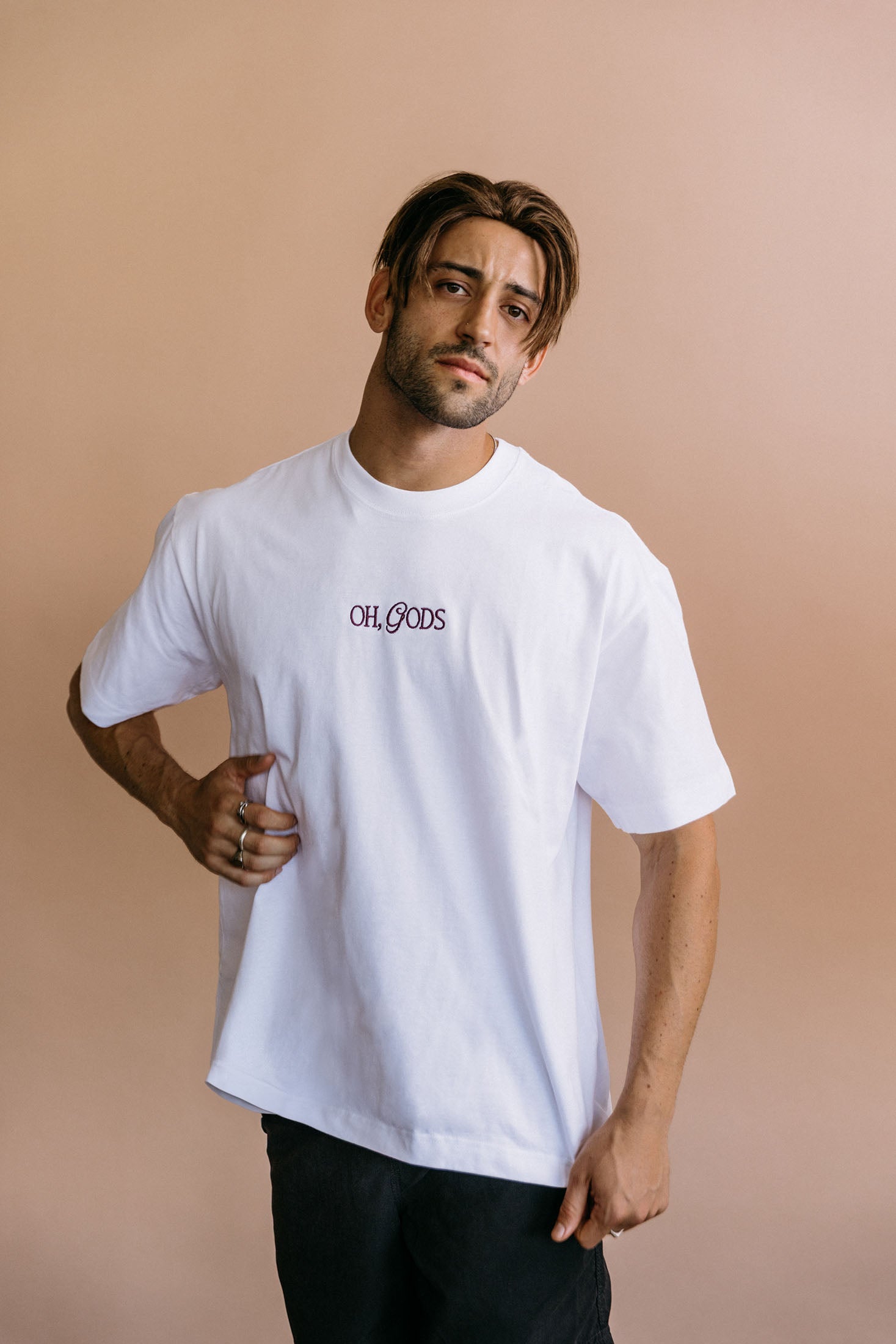 Male model wearing the white "Oh Gods" relaxed fit embroidered T-shirt by WNGSPN, with a relaxed silhouette and clean lines.