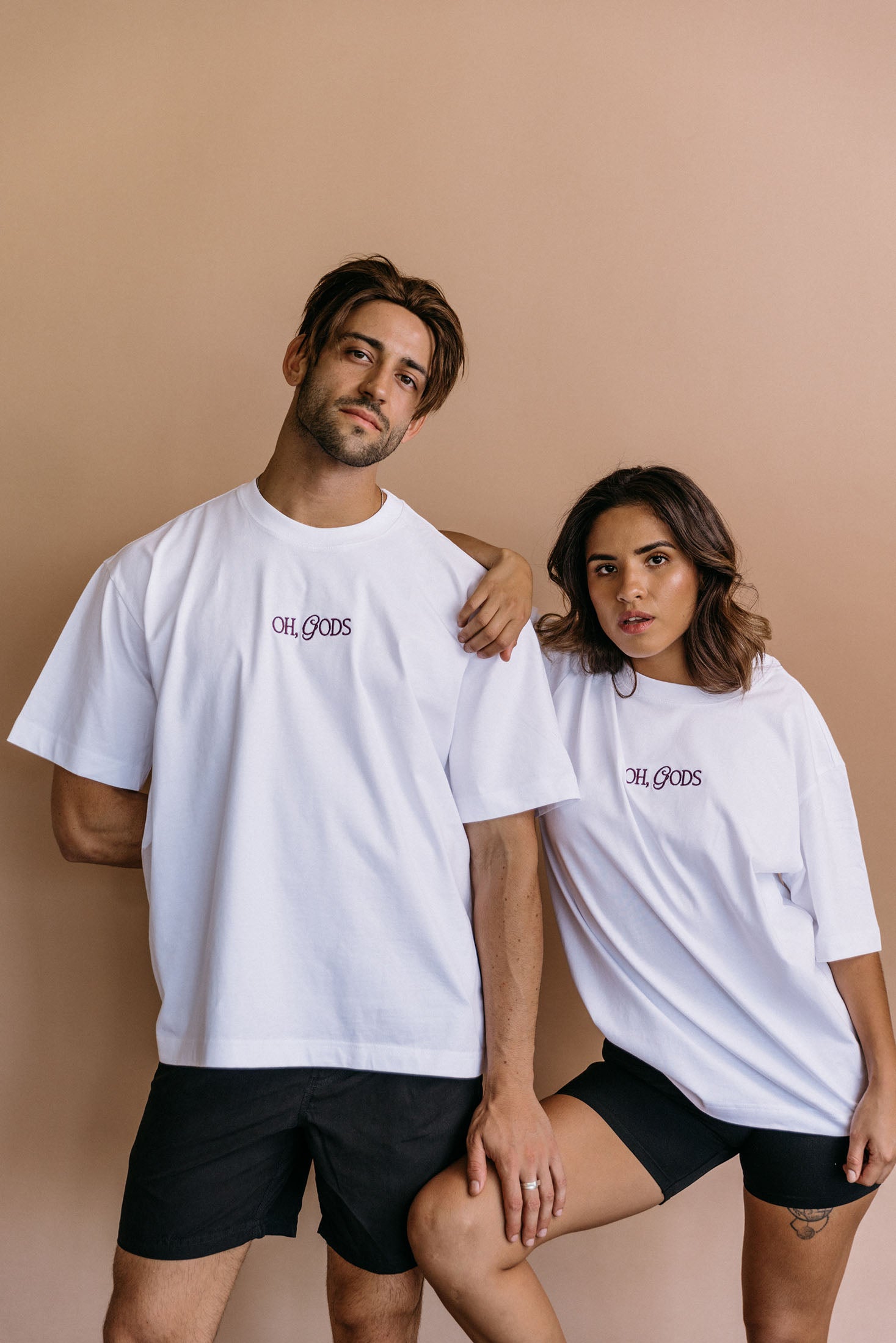 Couple wearing the white "Oh Gods" relaxed fit embroidered T-shirt by WNGSPN, with subtle tension and modern edge.