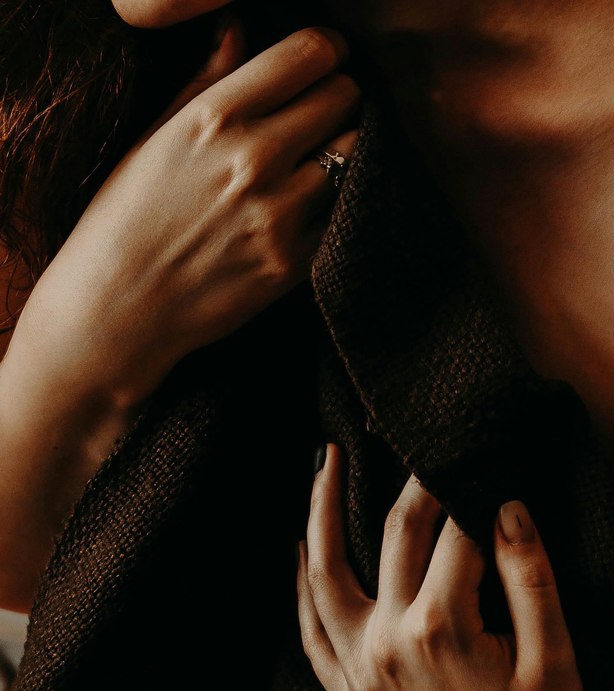 Close-up of hands holding fabric near the collarbone, capturing a moment of embodied emotion and sensual expression for WNGSPN