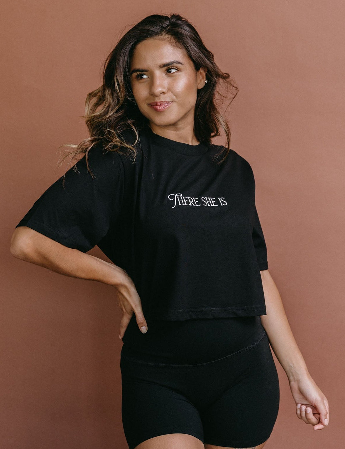 Female model wearing the black "There She Is" cropped embroidered T-shirt by WNGSPN, styled with understated confidence.