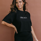 Female model wearing the black "There She Is" cropped embroidered T-shirt by WNGSPN, styled with understated confidence.