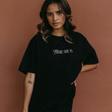 Female model wearing the black "There She Is" relaxed fit embroidered T-shirt by WNGSPN, styled with understated confidence.